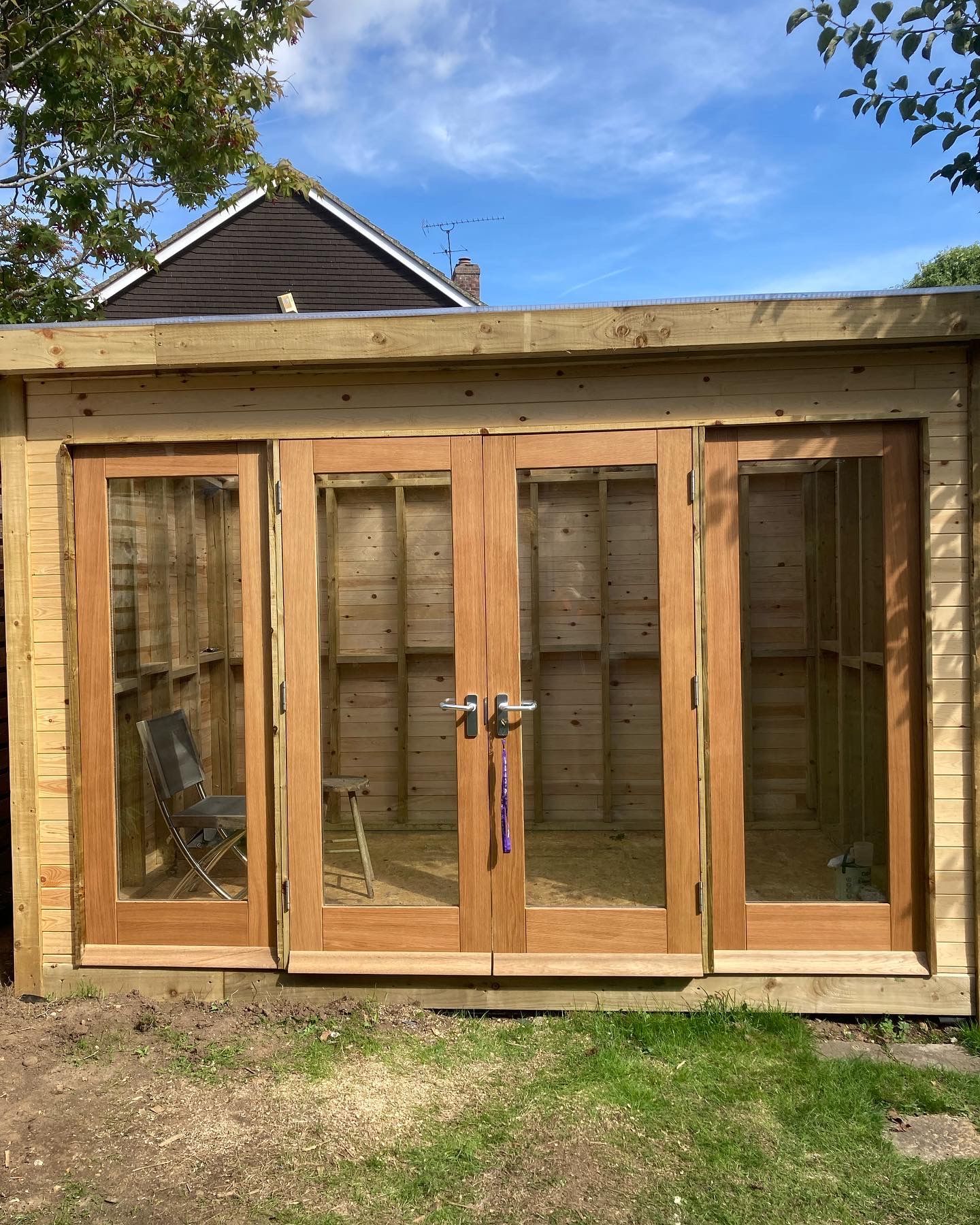 Wood-framed glass double doors on a small shed or garden building, with grass and trees around it.