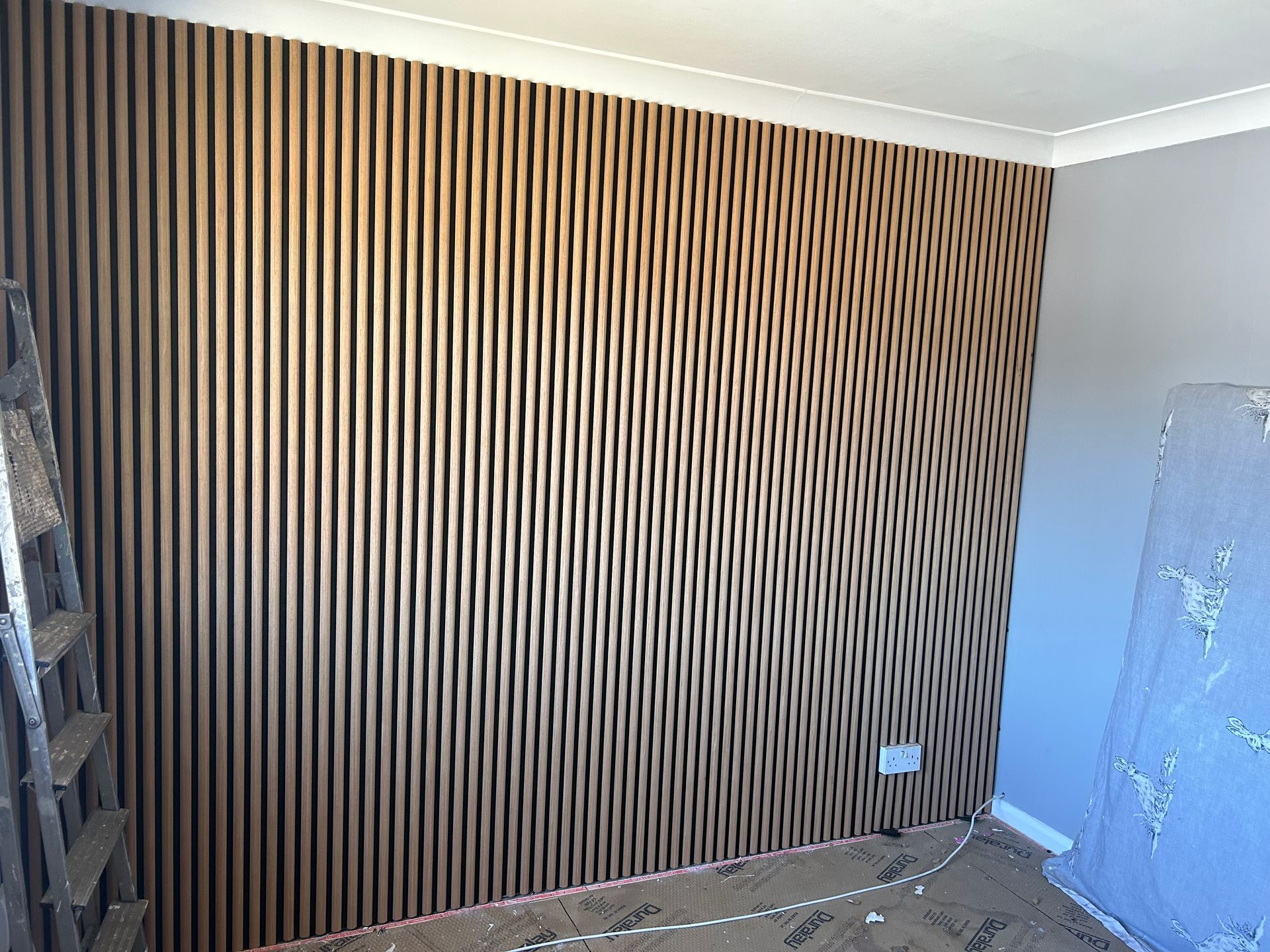 Interior wall with vertical wood slats, gray side wall, and a plastic-covered object in the corner.
