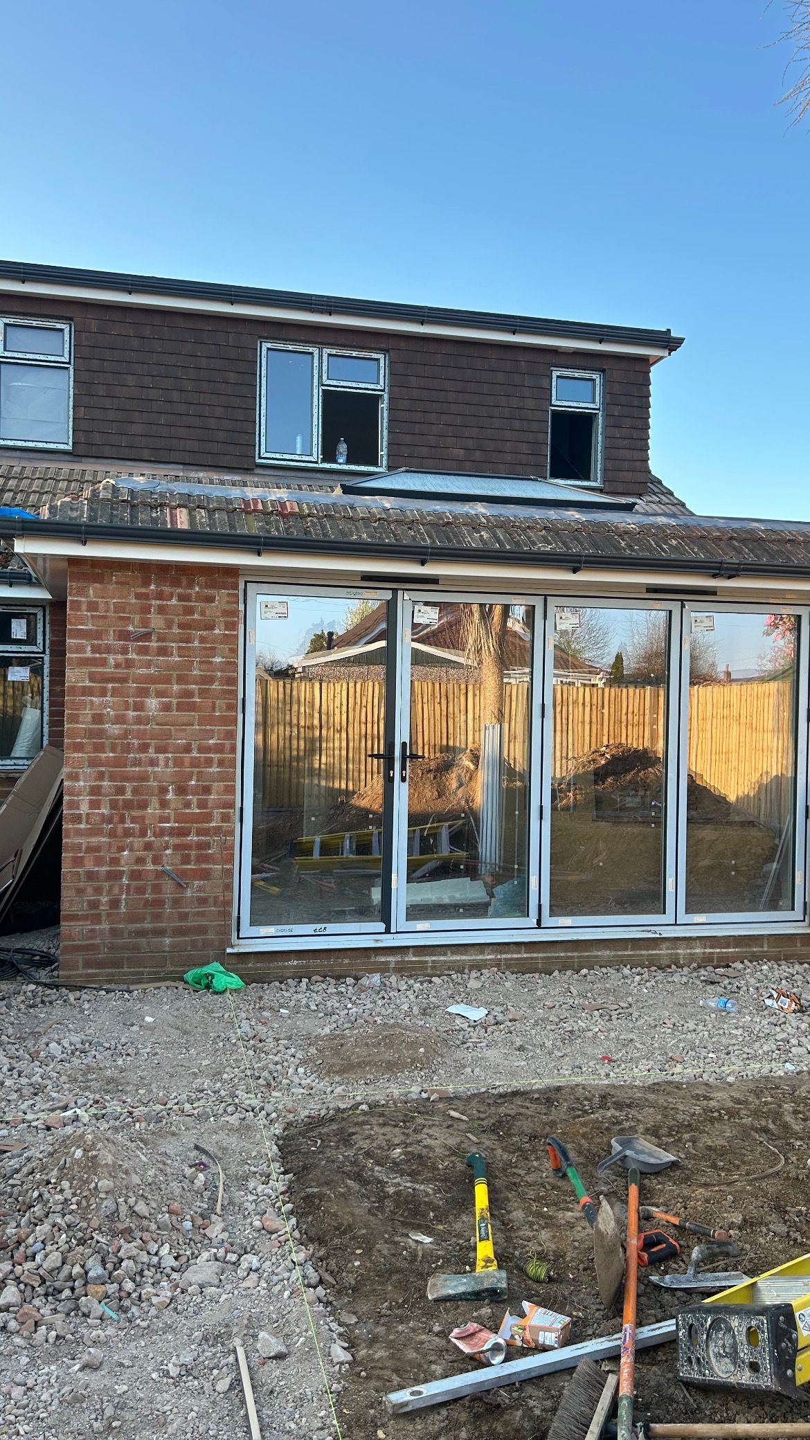 New house under construction with brick and dark siding, large glass doors, and gravel in front
