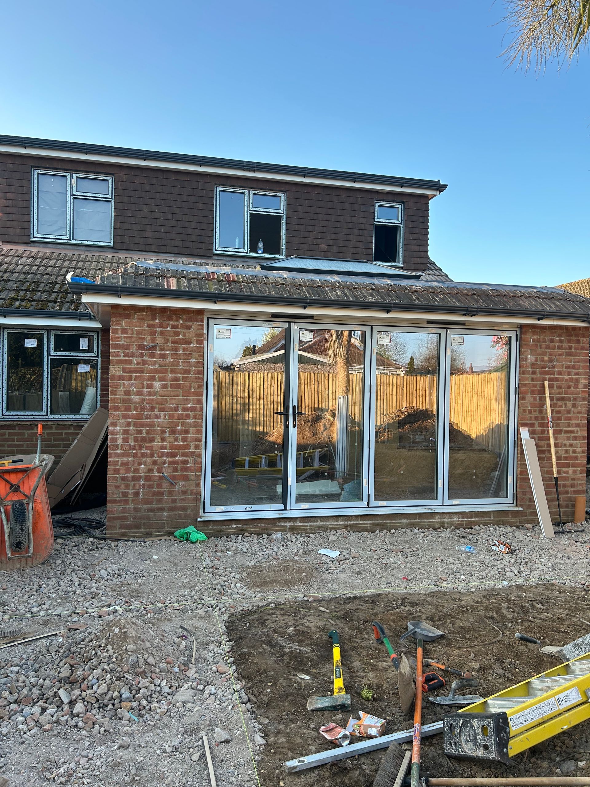 Brick house under renovation with large glass patio doors, gravel yard, and construction materials in front