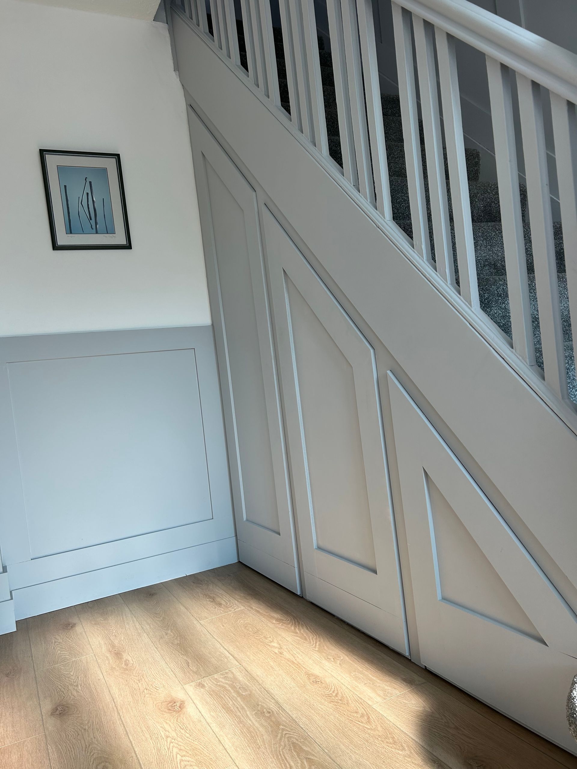 White staircase with diagonal railing, blue-gray wall paneling, and a small framed picture on a sunlit floor.