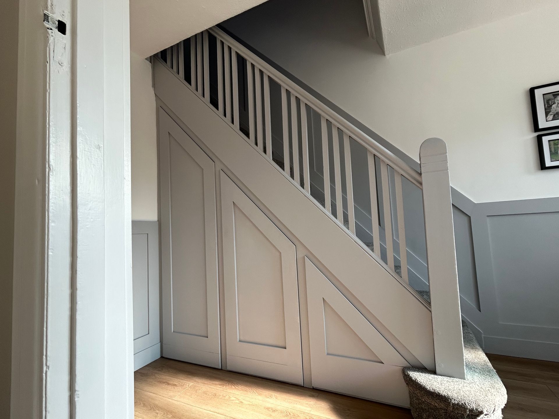 Under-stair storage with a slanted beige door and vertical slats in a hallway