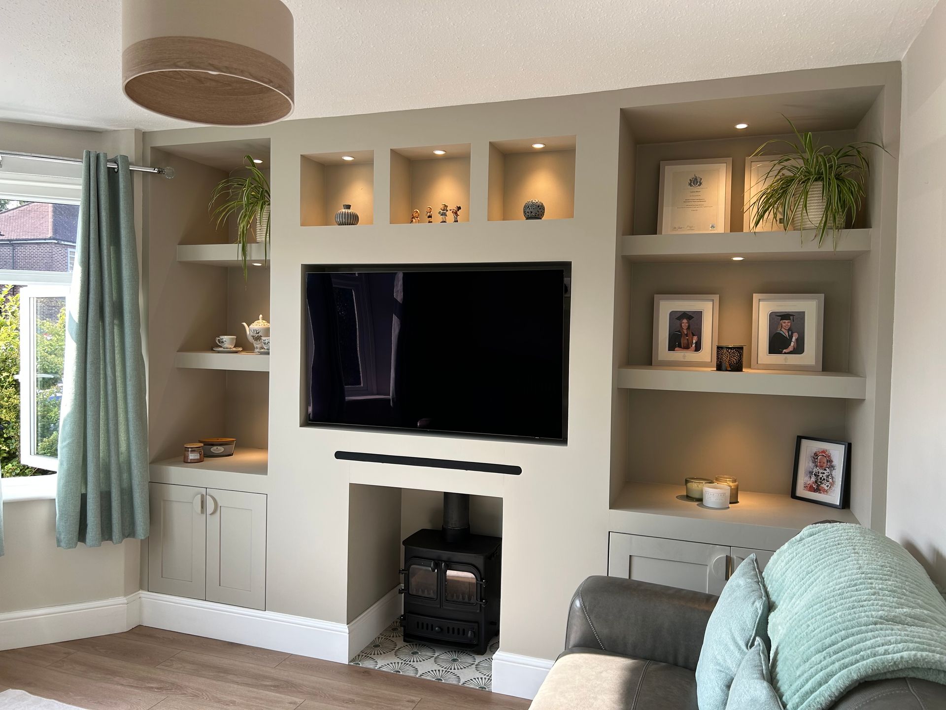 Modern living room with built-in shelves, a wall-mounted TV, small fireplace, and mint-green curtains.