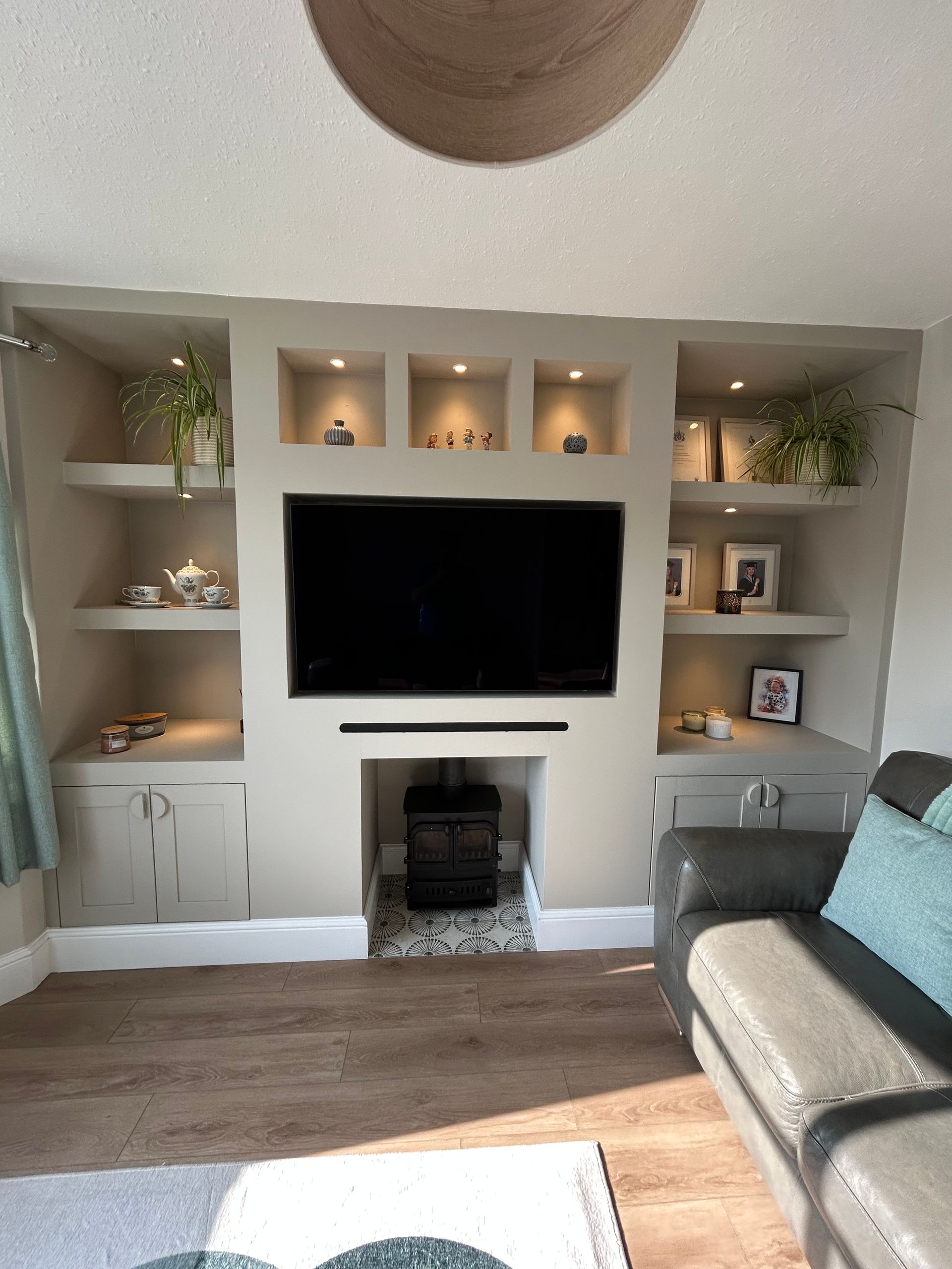 Modern living room with built-in shelves, wall-mounted TV, fireplace, gray sofa, and sunlight on wood floor