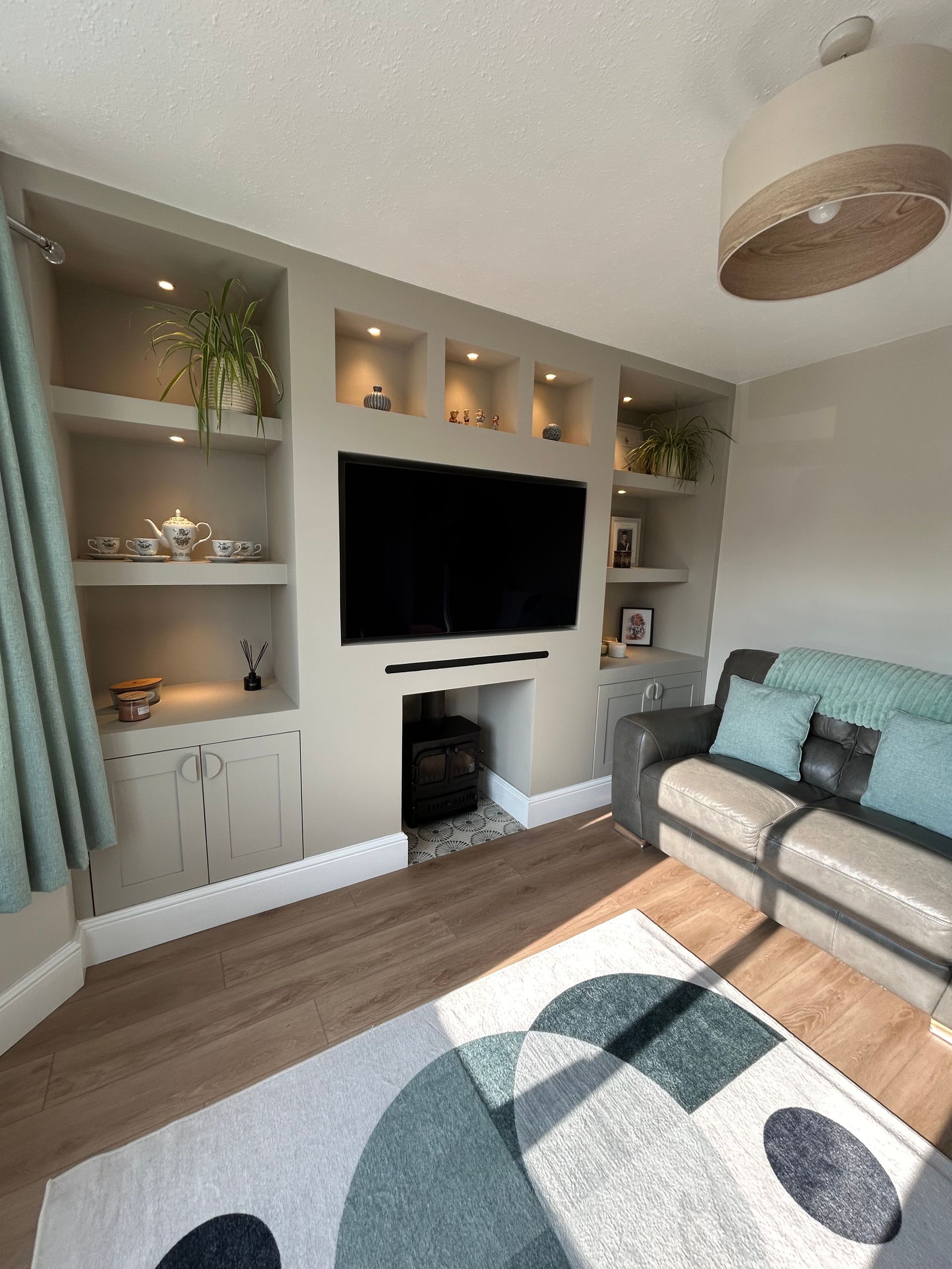 Bright living room with built-in shelves, wall-mounted TV, fireplace, gray sofa, and patterned rug.