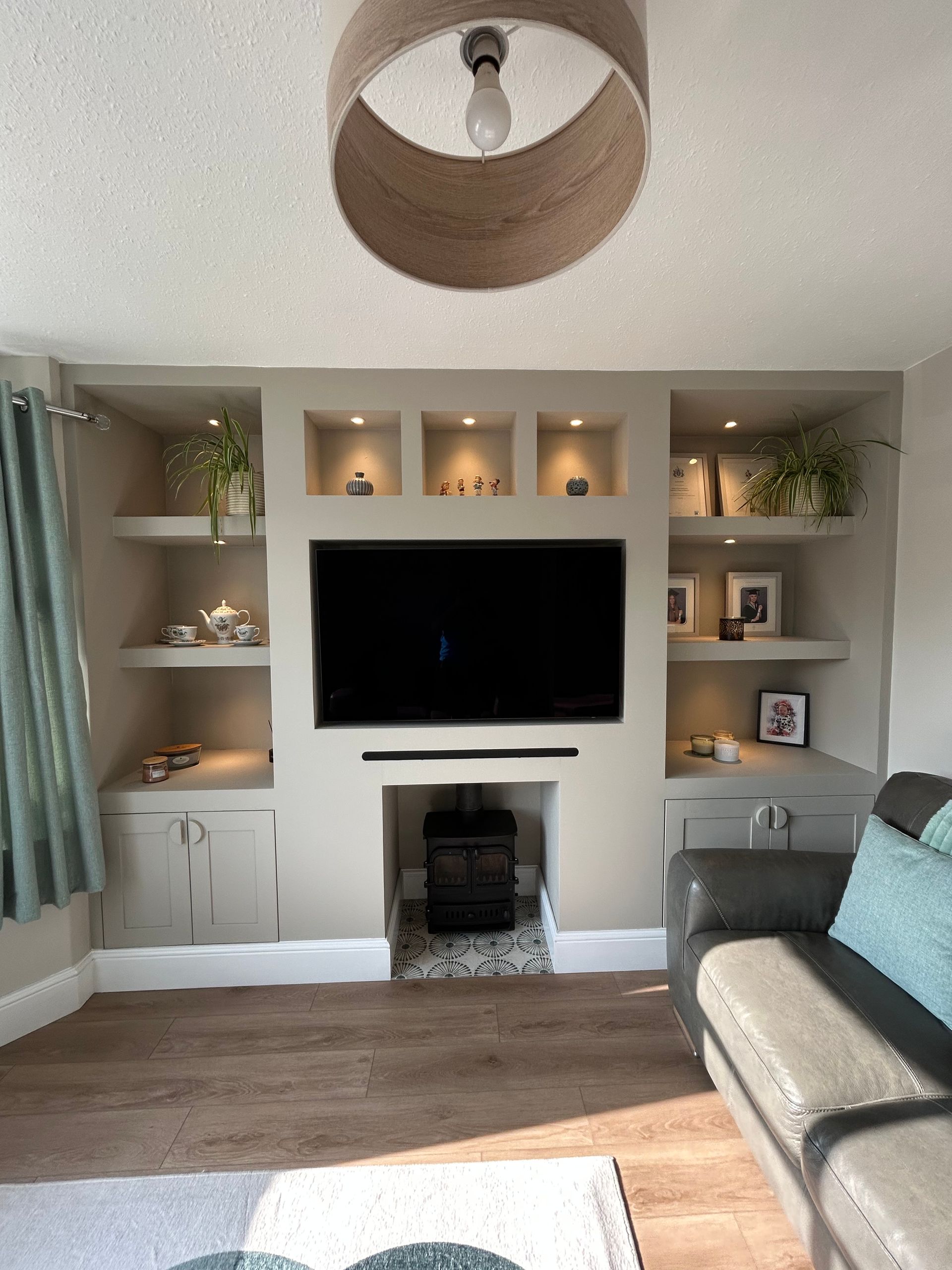 Living room with wall-mounted TV, built-in shelves, fireplace, and gray sofa in a bright windowed corner