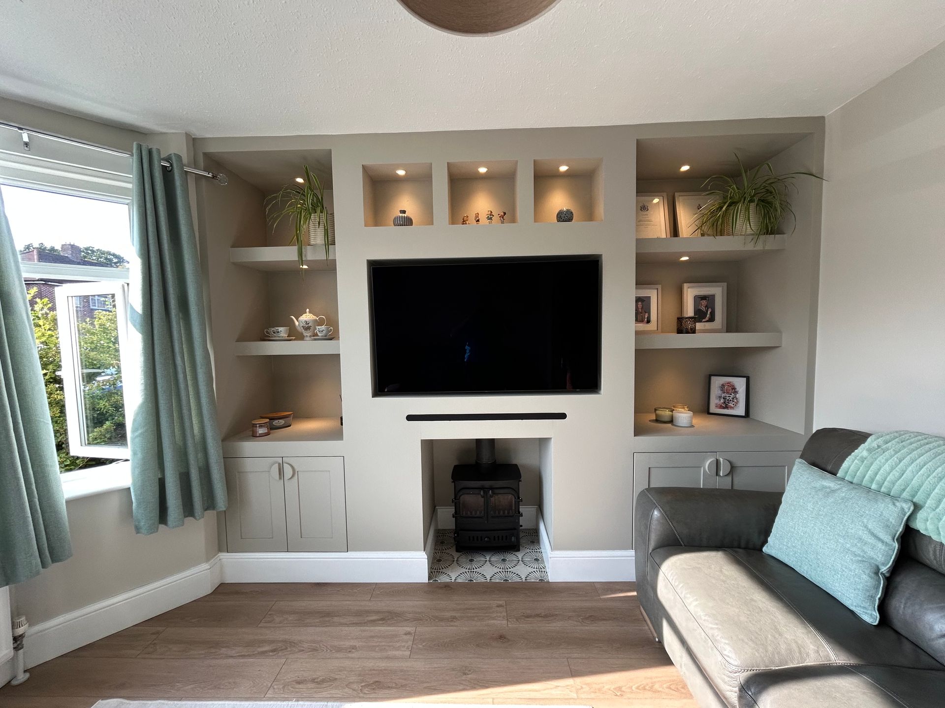 Bright living room with built-in shelves, wall TV, fireplace, teal curtains, and gray sofa