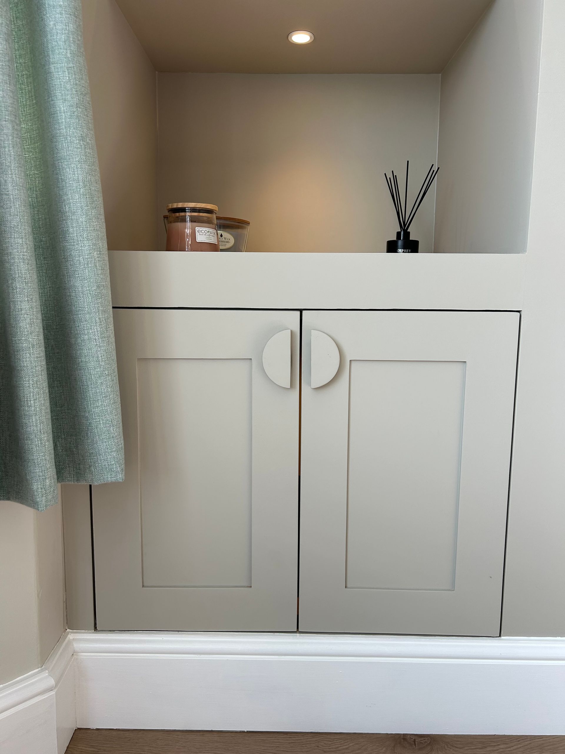 Built-in bathroom cabinet with white doors, countertop items, and a hanging curtain.