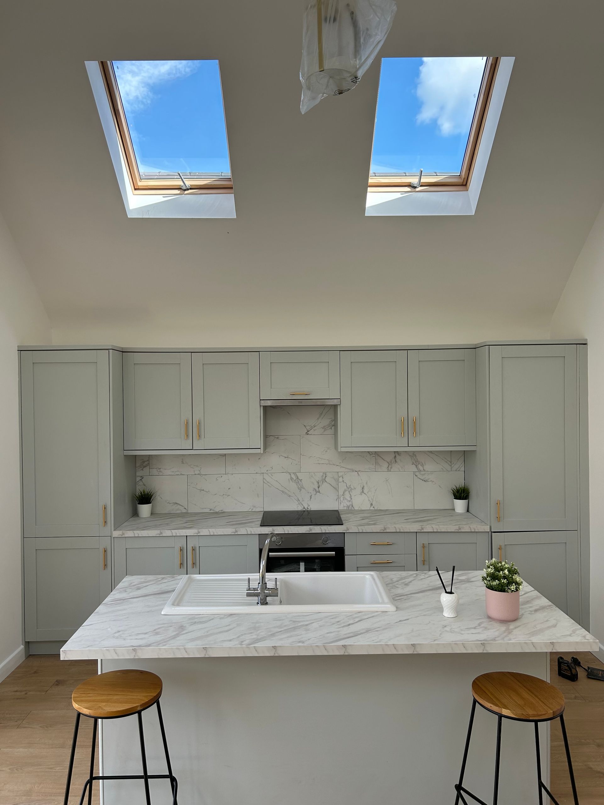 Bright modern kitchen with marble island, two stools, white cabinets, and skylight windows.