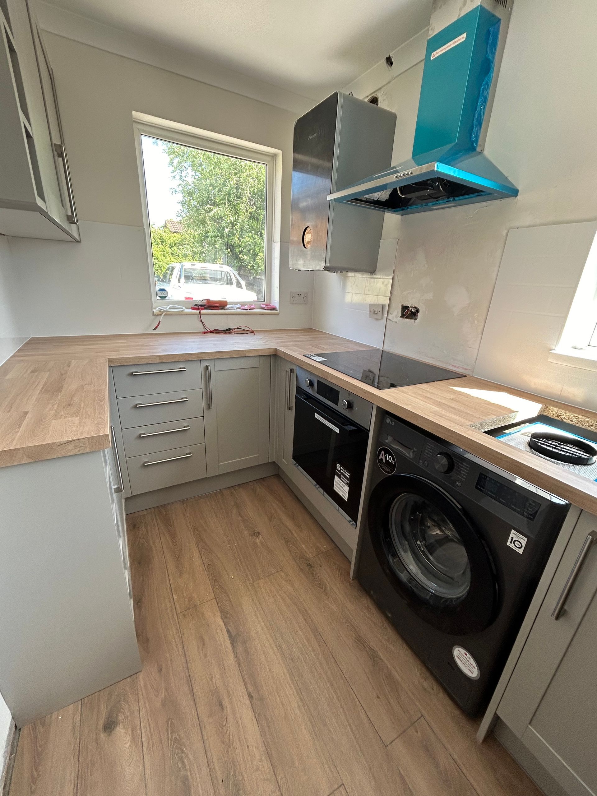 Compact modern kitchen with wood countertops, grey cabinets, and a washing machine under the counter.