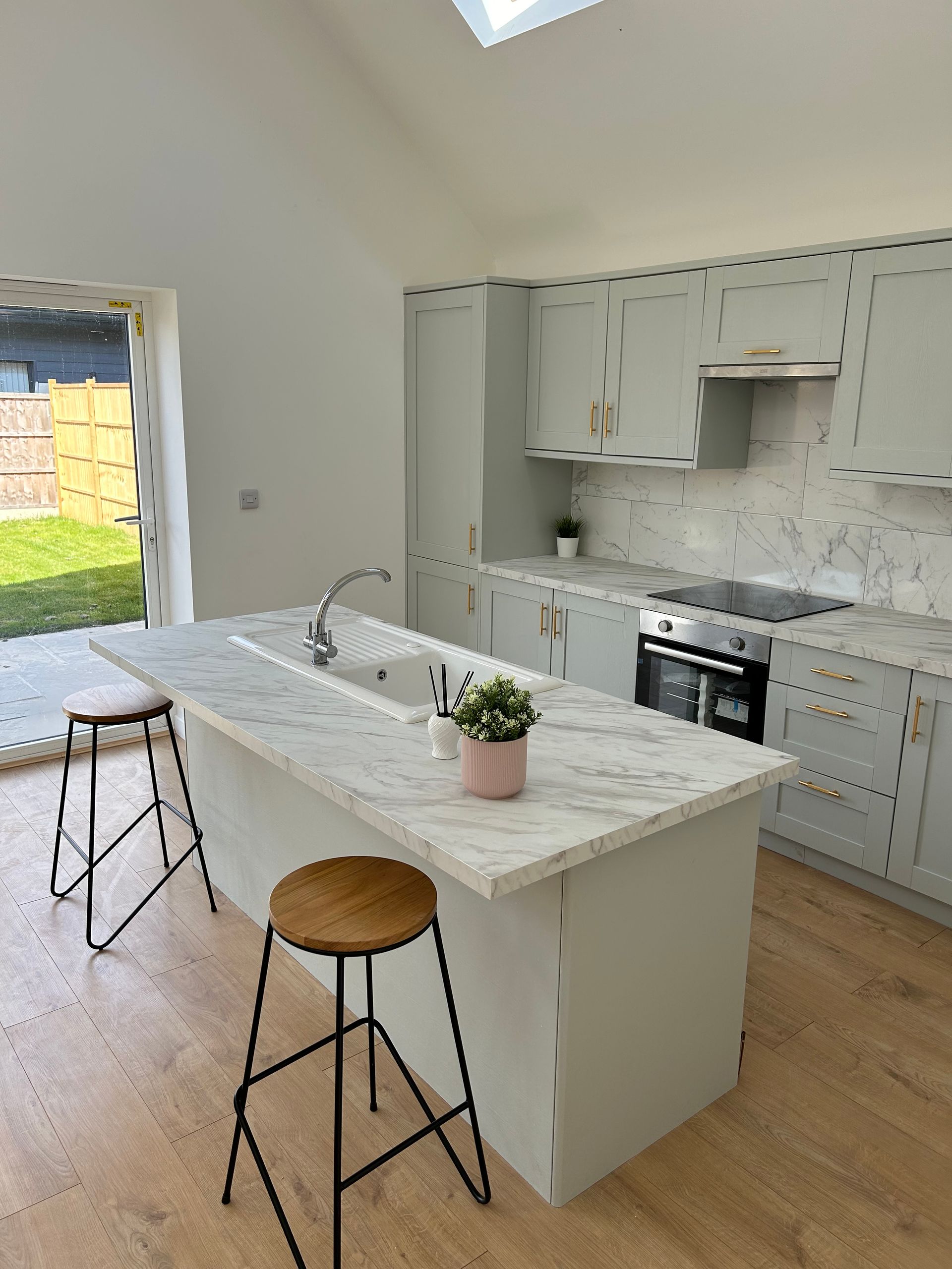 Bright modern kitchen with white cabinets, marble island, and two stools beside open patio doors