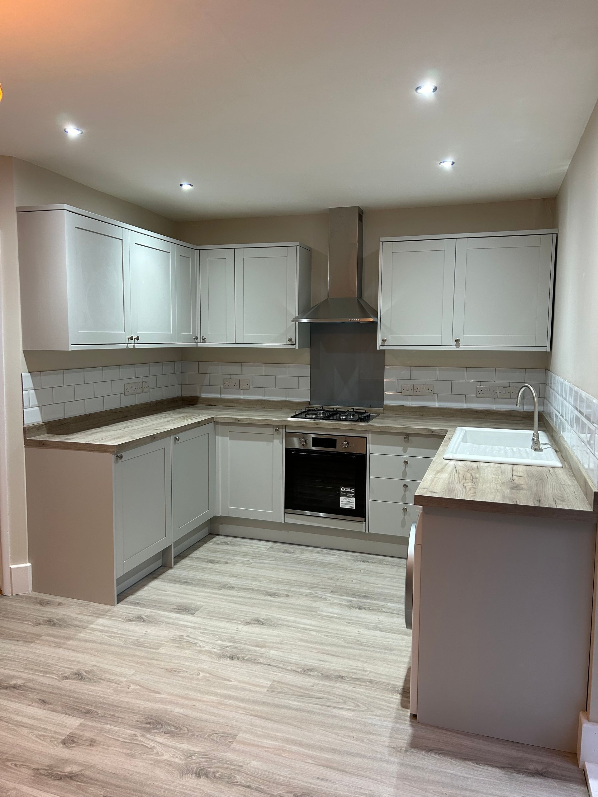 Empty modern kitchen with white cabinets, gray countertops, and recessed ceiling lights.