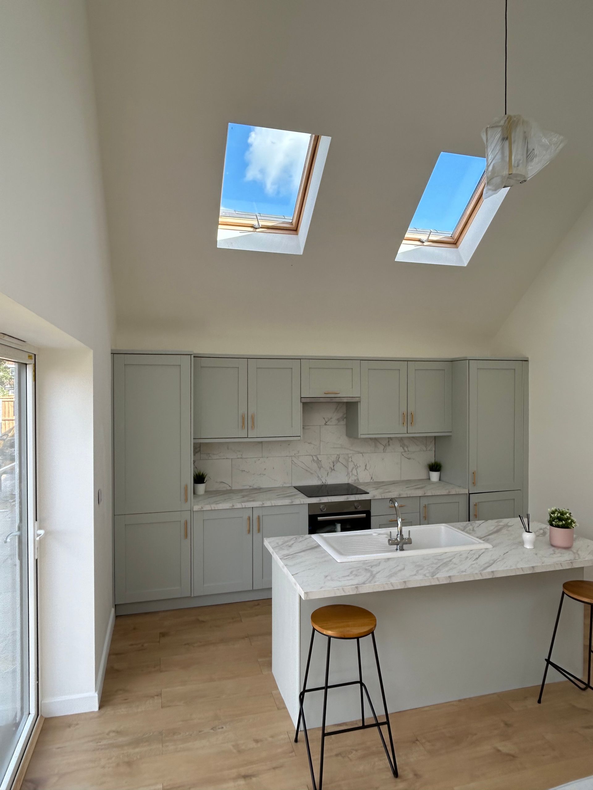 Bright modern kitchen with white cabinets, marble island, wood floors, and two skylight windows.