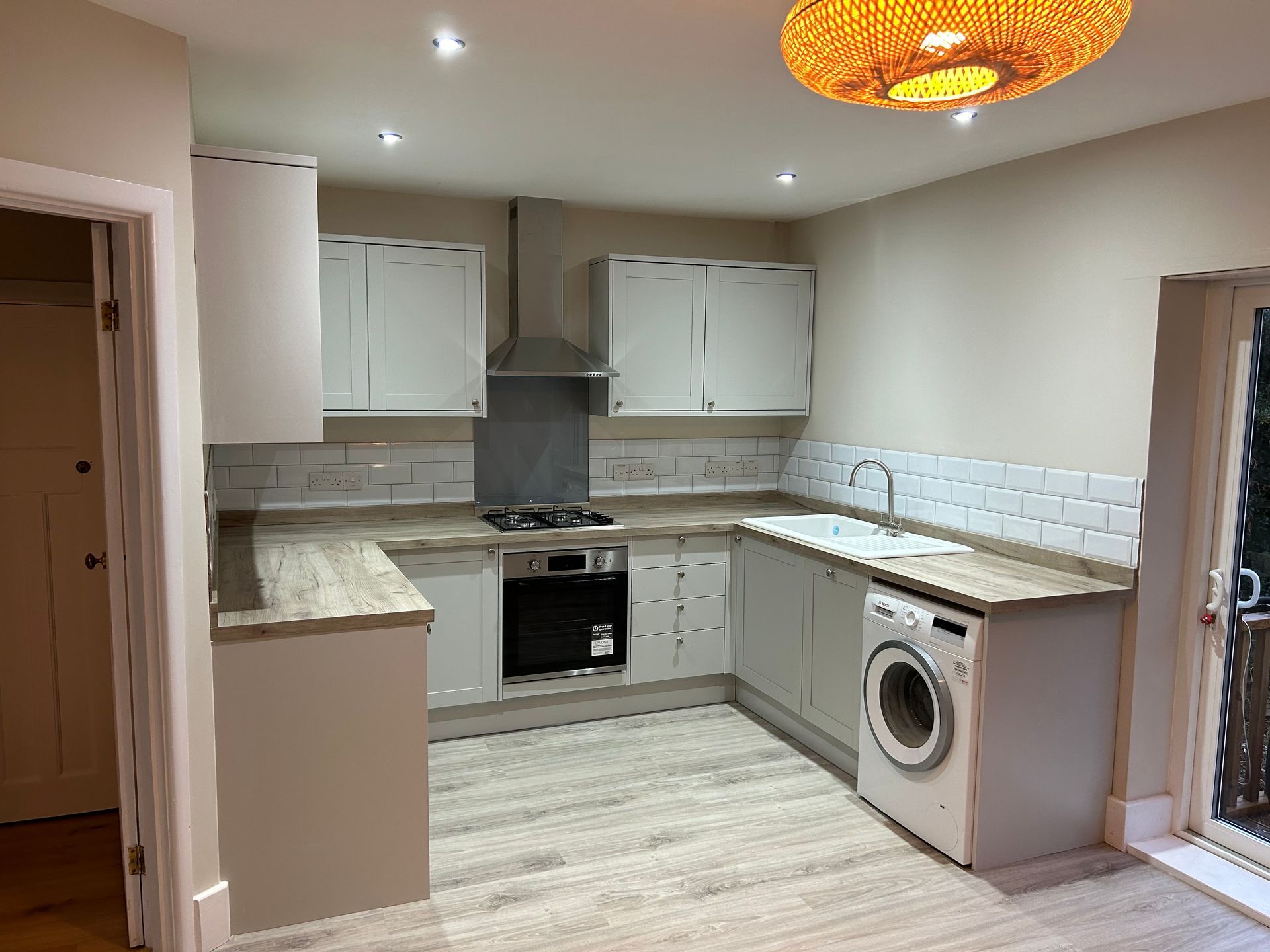 Bright, modern kitchen with white cabinets, gray countertops, oven, and washing machine near sliding doors
