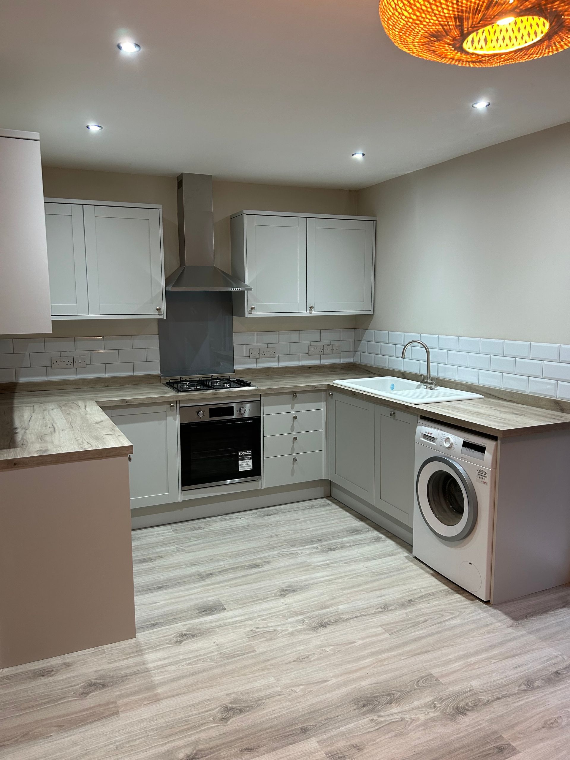 Modern kitchen with white cabinets, light wood floors, built-in oven, and a washing machine under the counter