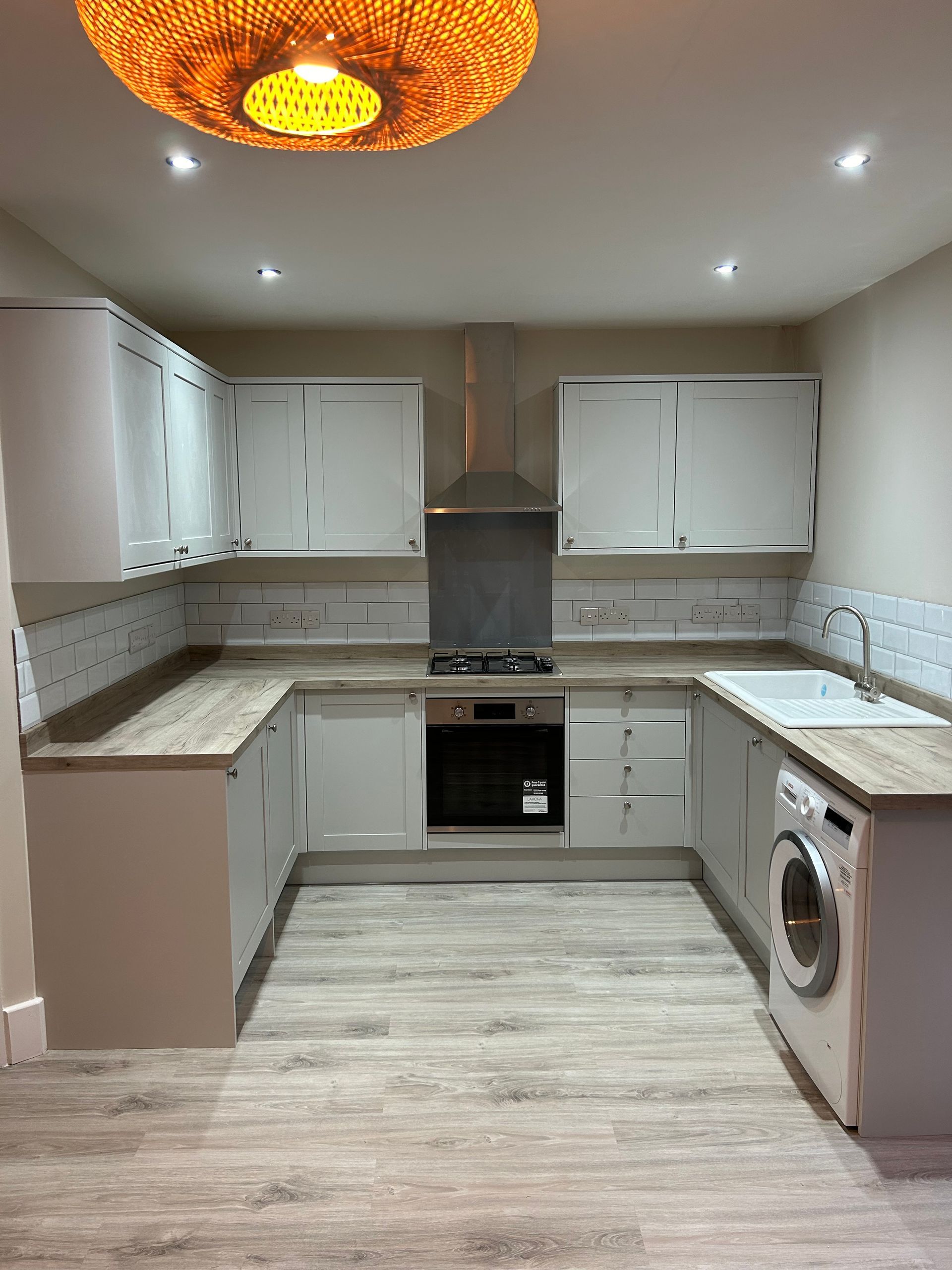 Modern U-shaped kitchen with white cabinets, gray countertops, stove, washer, and orange ceiling light.