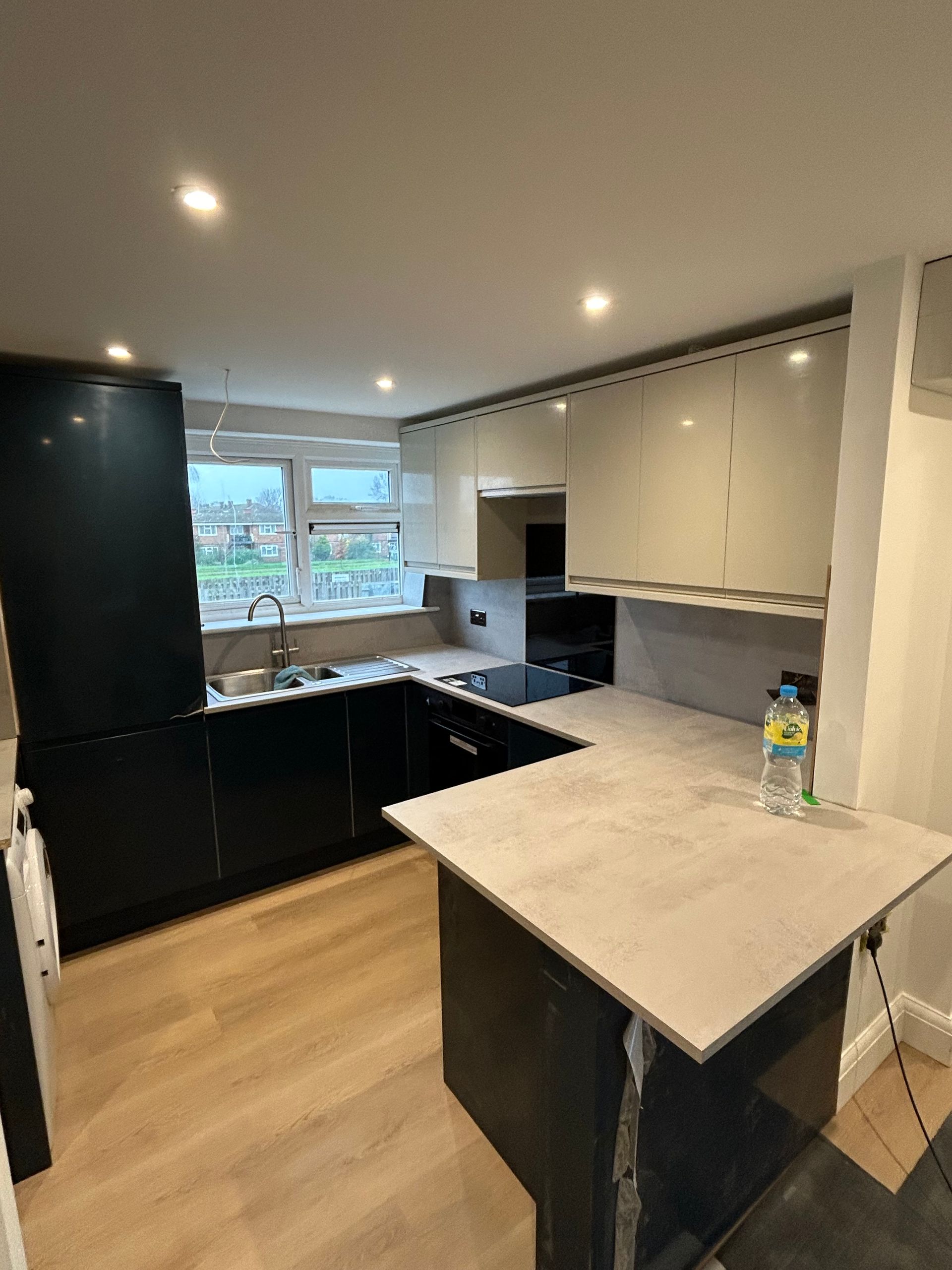 Modern kitchen with black cabinets, white countertops, wood floor, and a window over the sink
