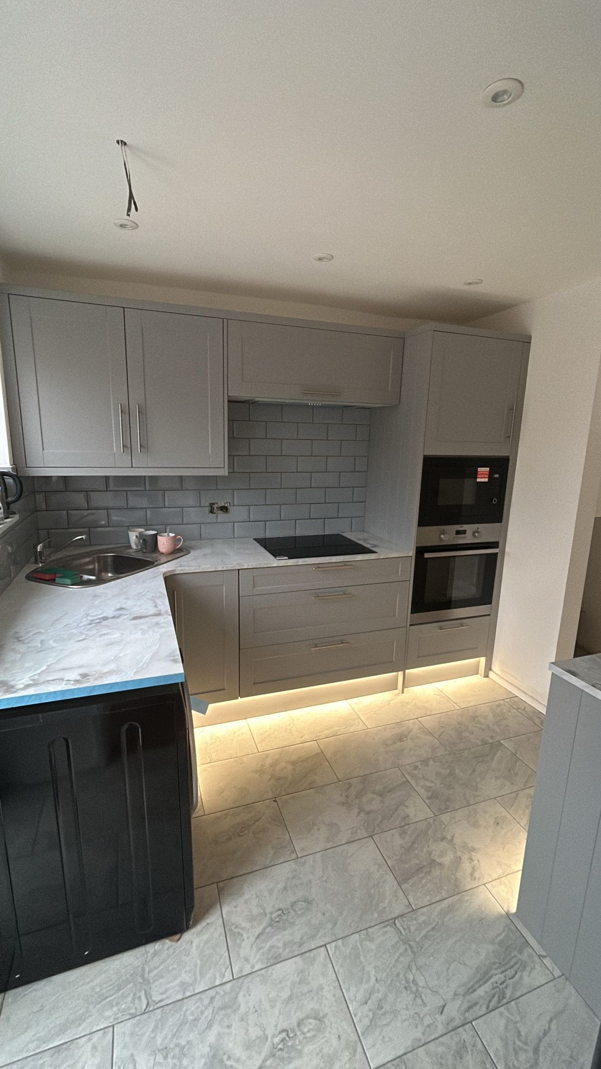 Modern kitchen with white cabinets, gray backsplash, built-in ovens, and under-cabinet lighting