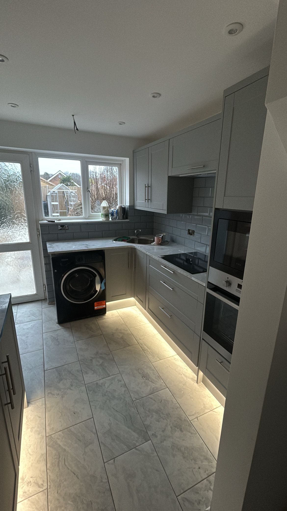 Bright modern kitchen with white cabinets, tiled floor, and a washing machine near a window.