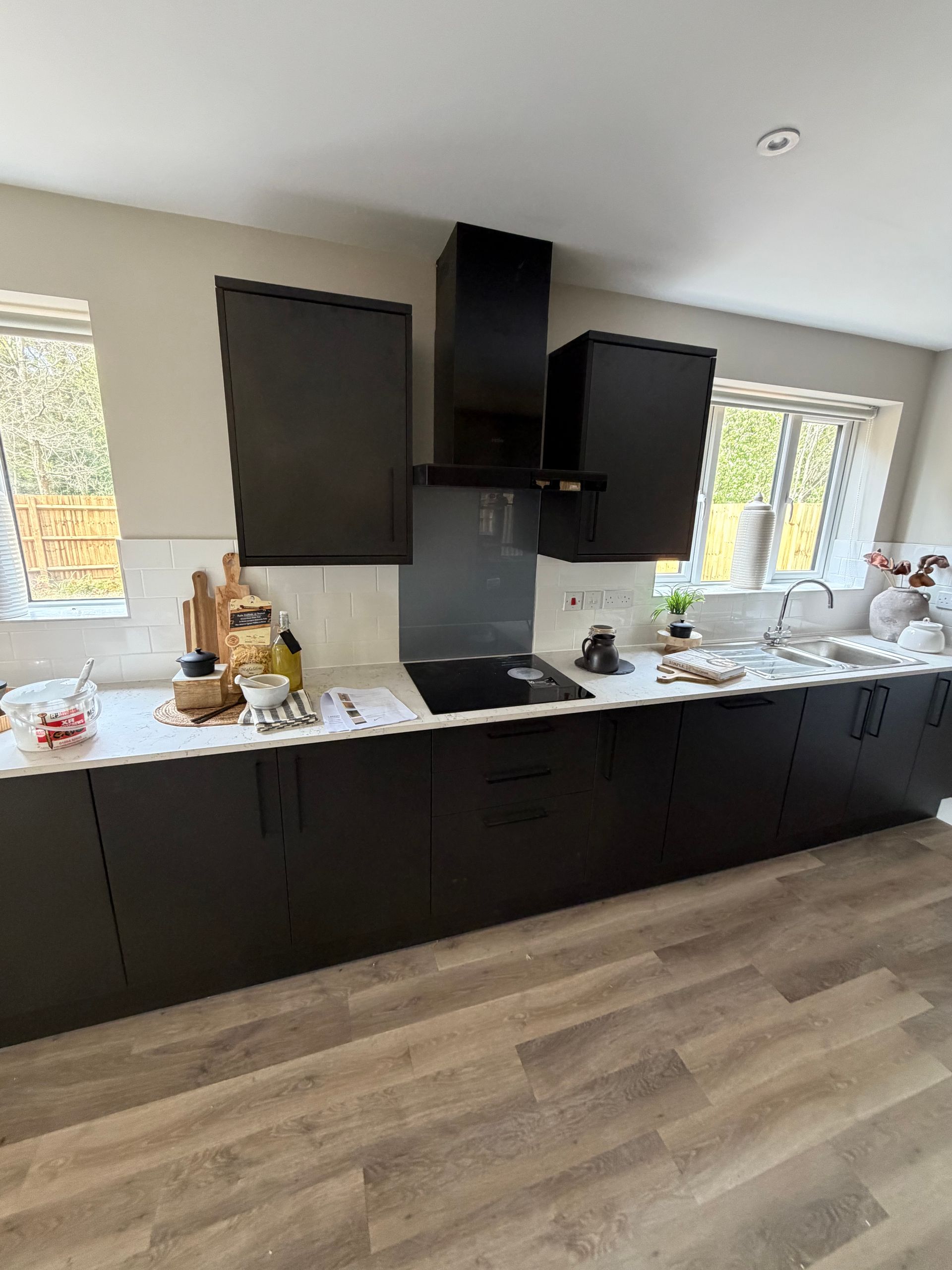 Modern kitchen with dark cabinets, white countertops, and light wood flooring, with windows on either side.