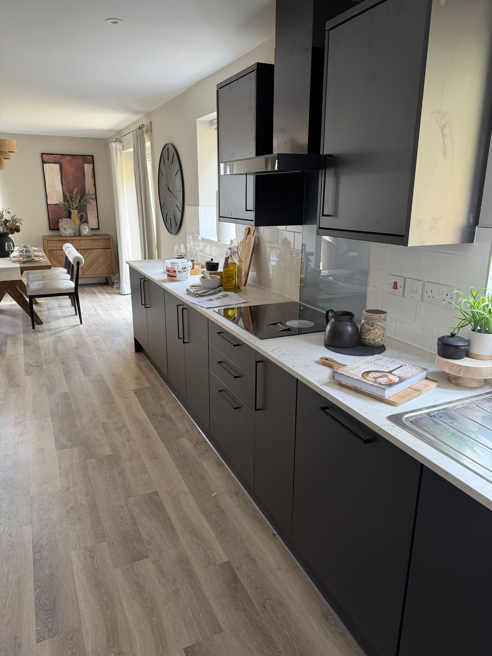 Modern kitchen with dark cabinets, white countertop, and wood flooring leading to a living area