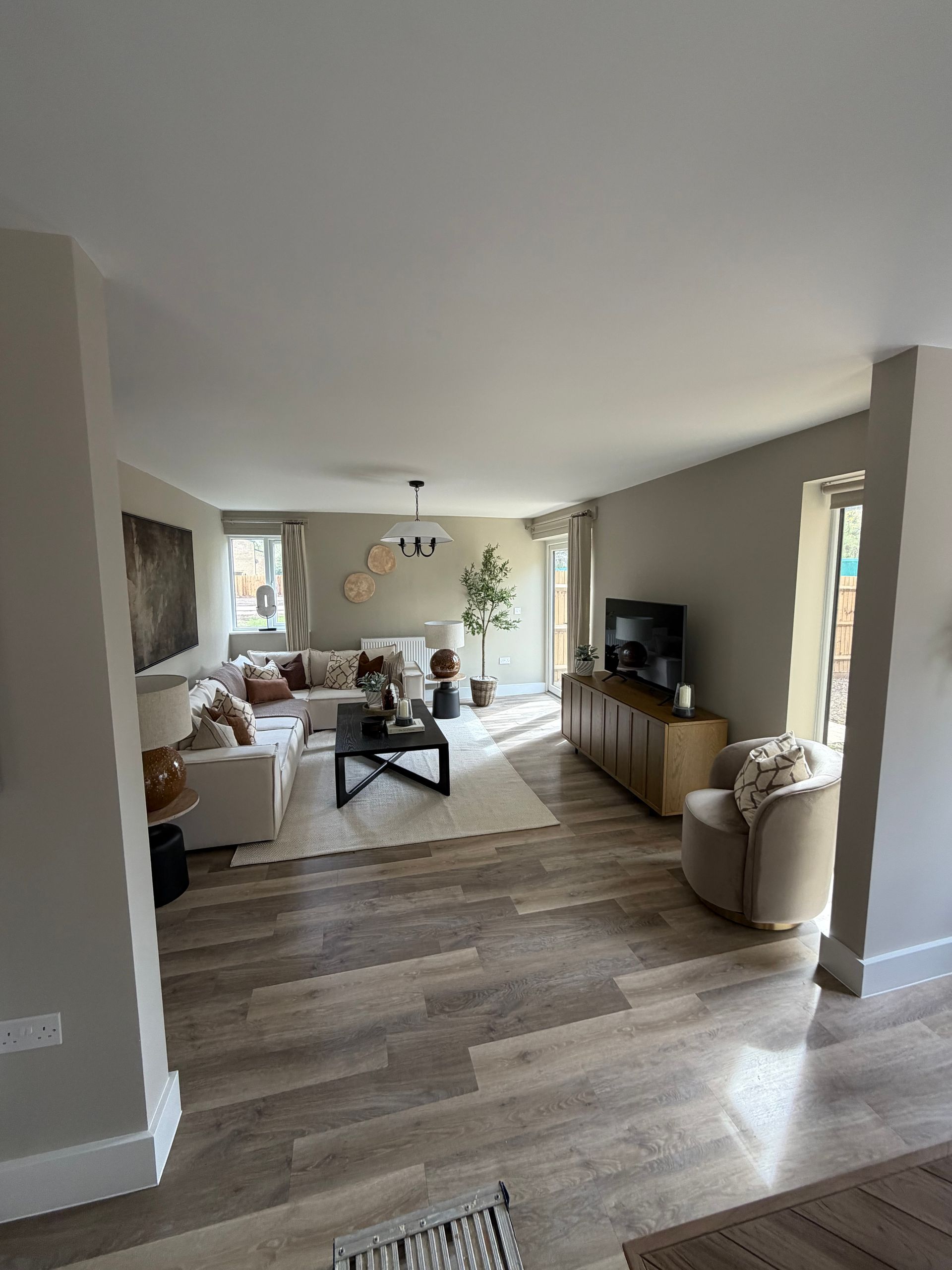 Bright living room with gray walls, wood floors, white sofas, and a TV on a wooden console.