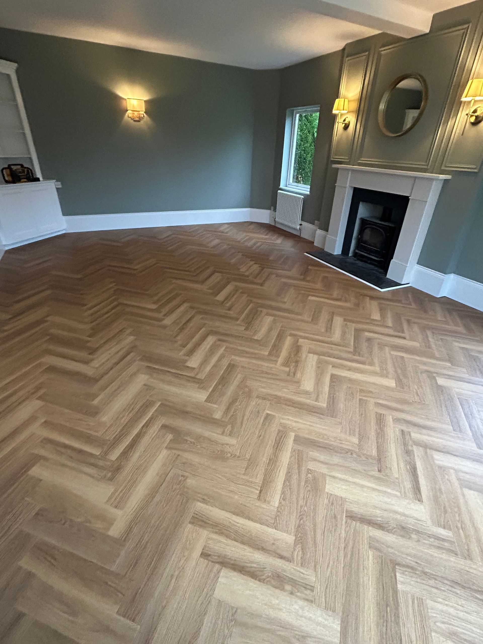 Empty living room with herringbone wood floor, dark green walls, fireplace, and wall sconces.