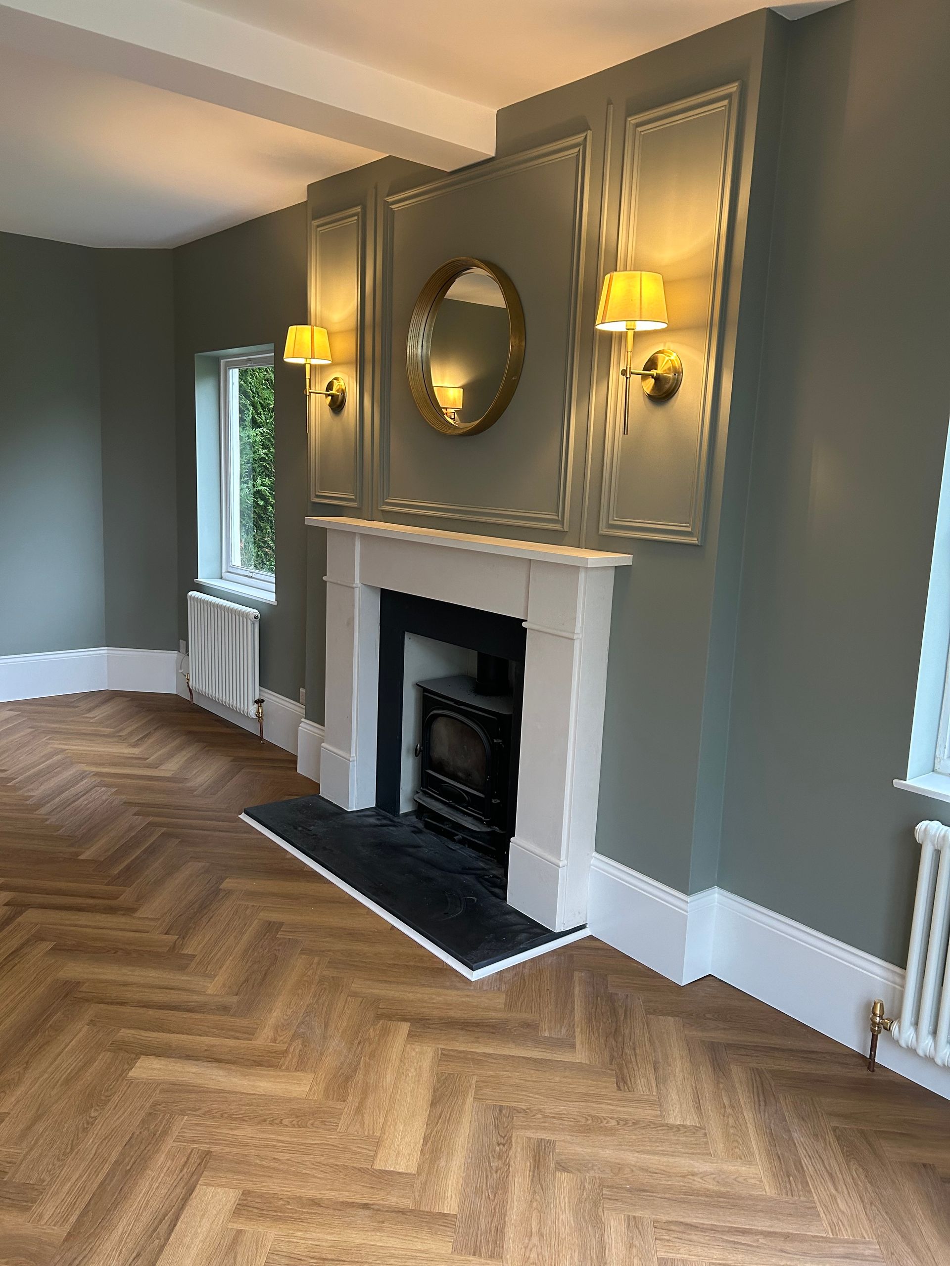Elegant living room with gray walls, herringbone wood floor, fireplace, wall sconces, and oval mirror.