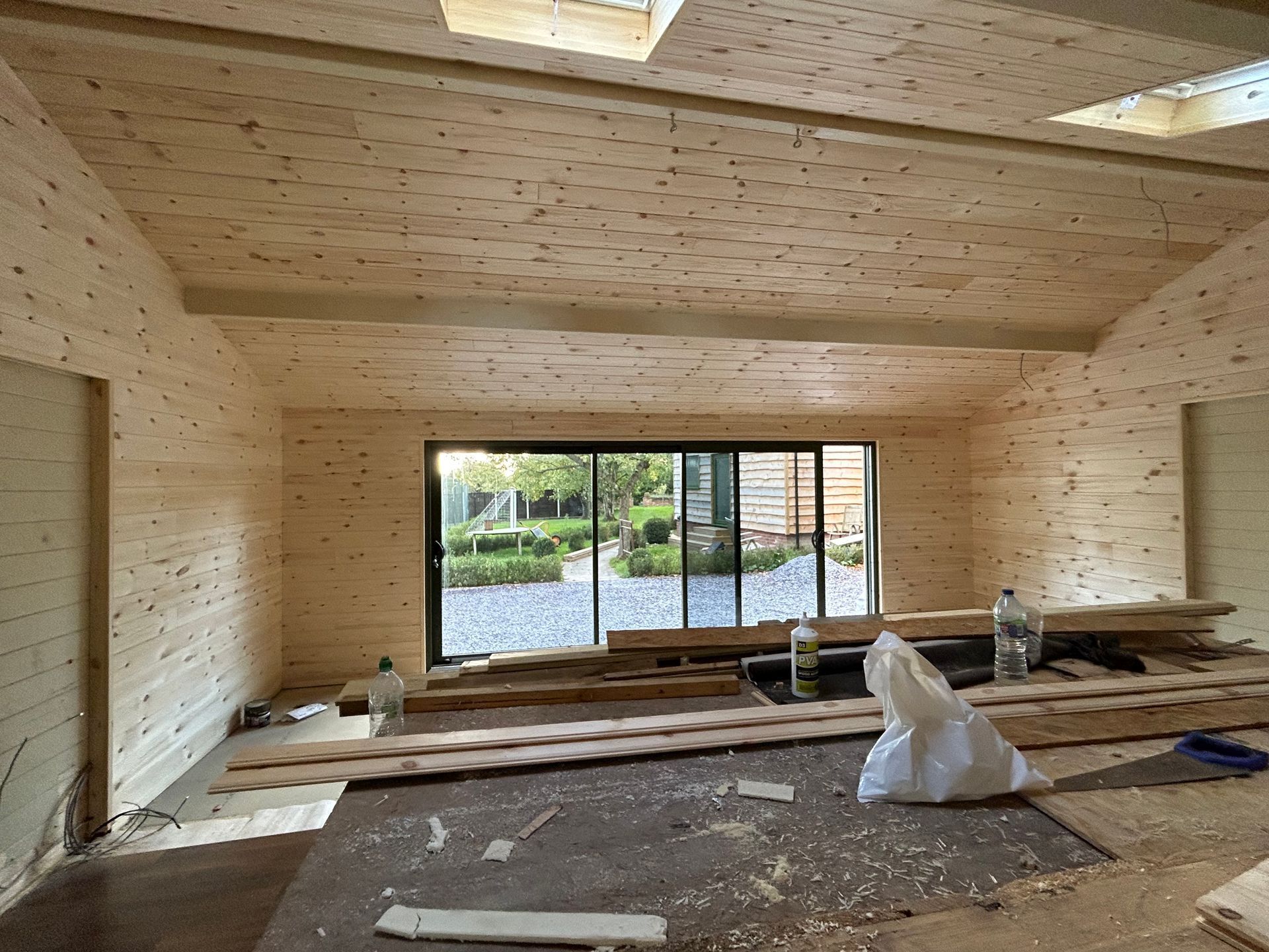 Empty unfinished wooden room with large sliding glass doors and construction materials on the floor