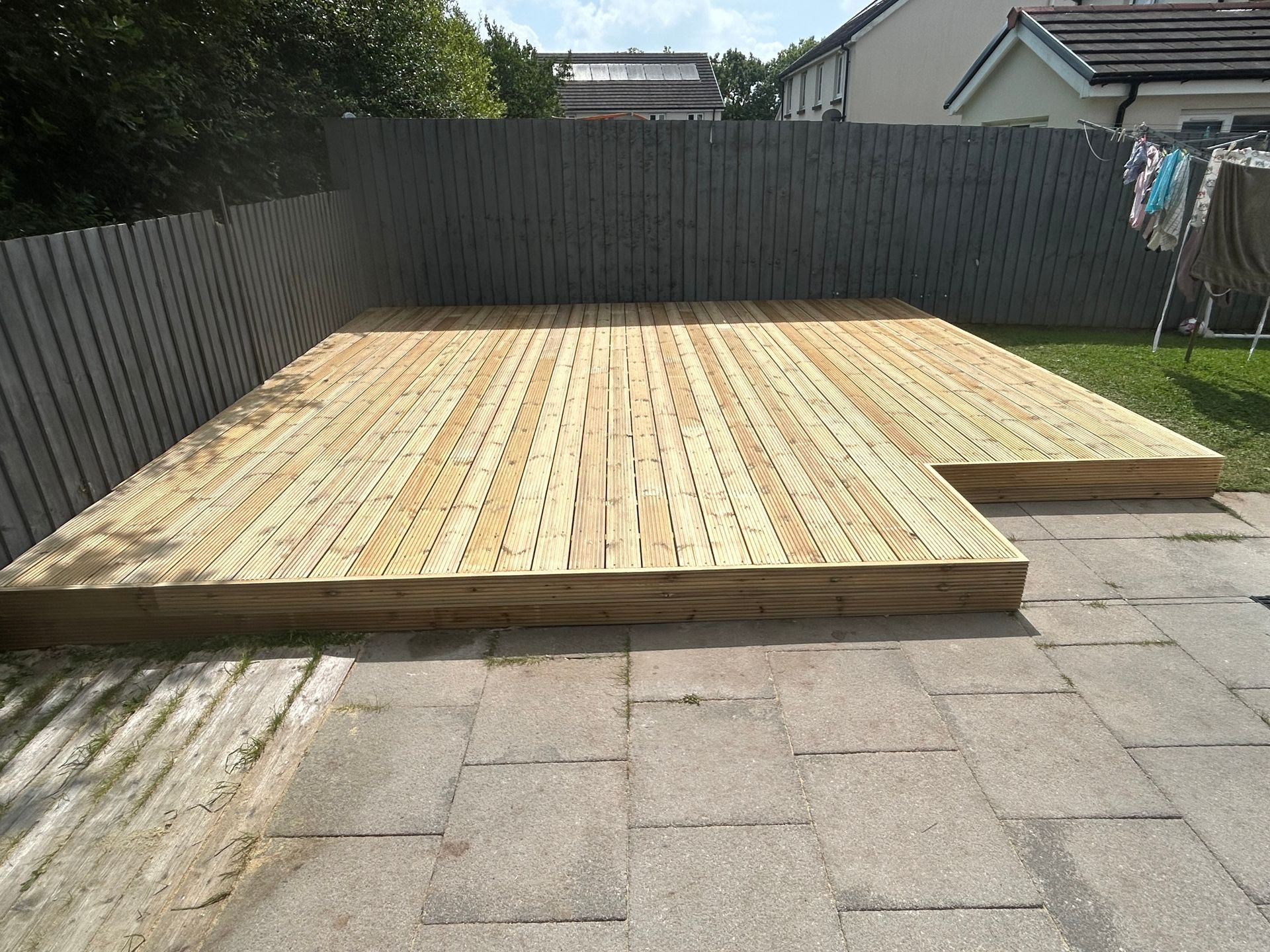 Wooden deck platform under construction in a fenced backyard on a paved patio