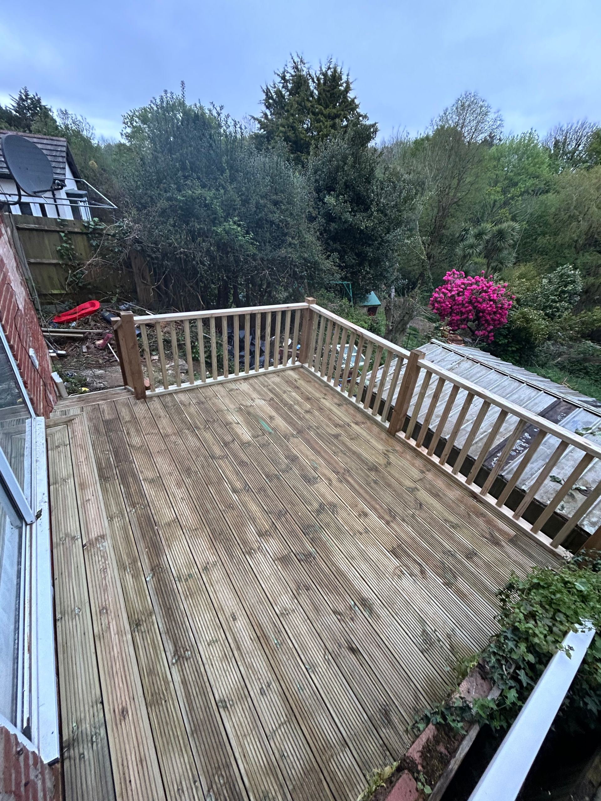 Wooden rooftop deck with railing, overlooking trees and a pink flowering shrub