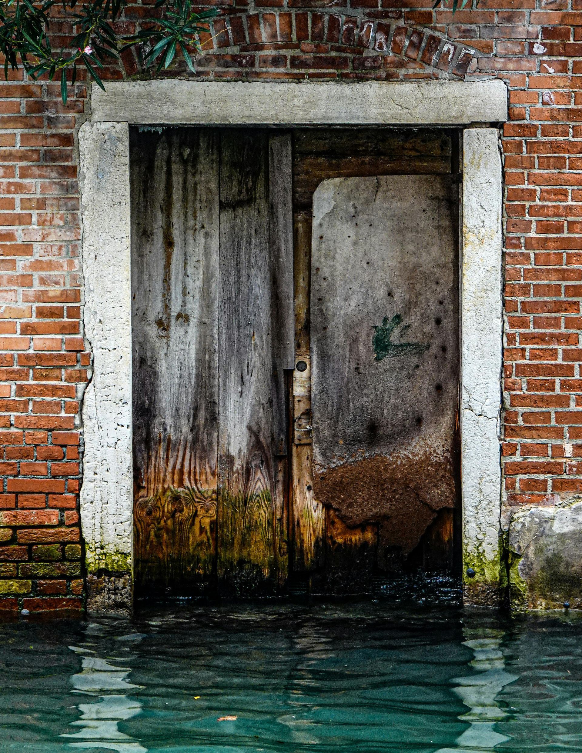 Water-logged wooden door in weathered brick wall. Water level high, possibly Venice, Italy.