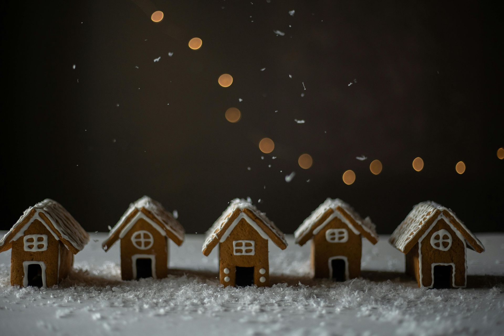 Five gingerbread houses in snow, against a dark background with glowing lights above.