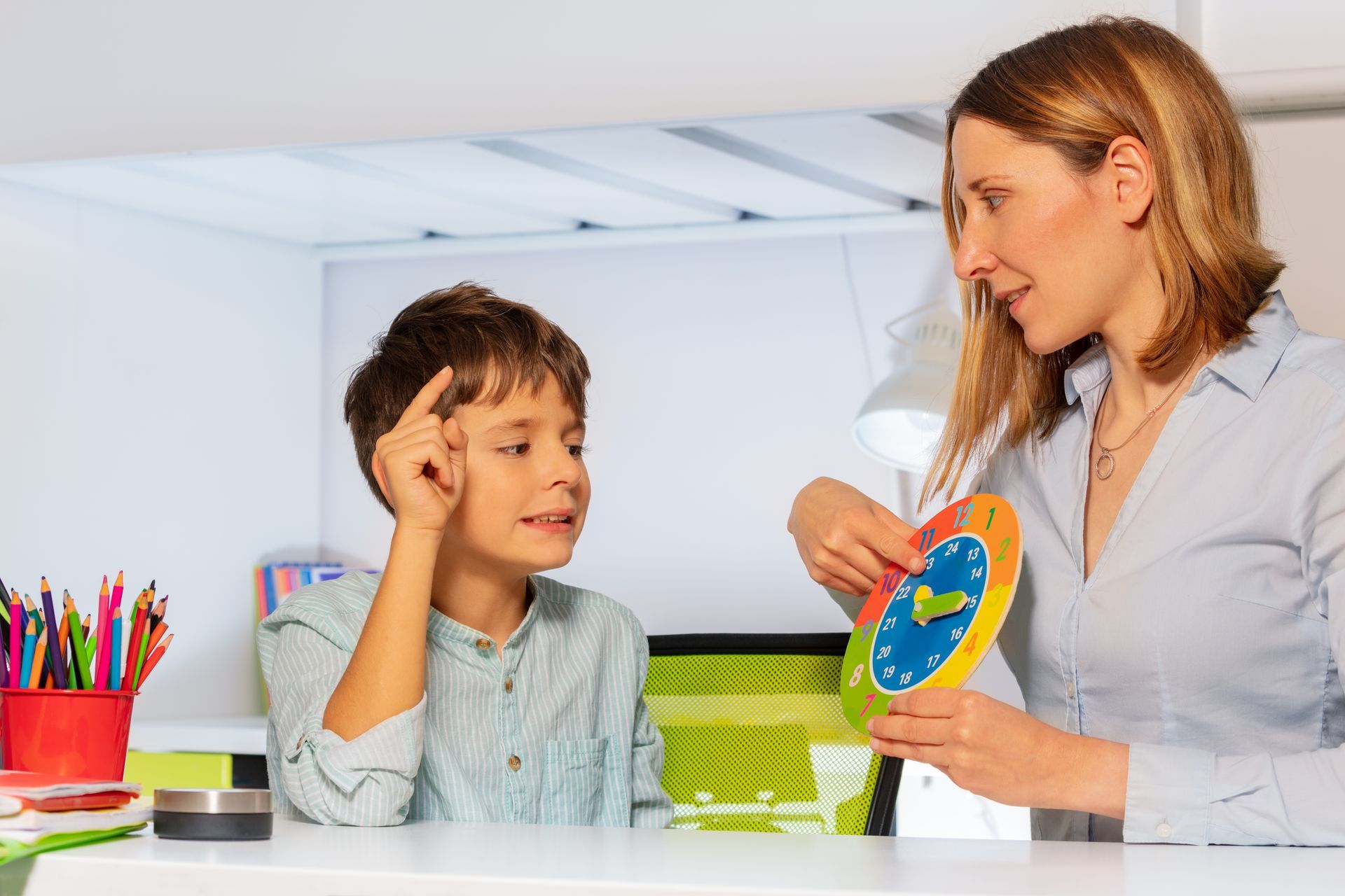 Woman teaching boy about time using a clock, indoors. Woman teaching boy about time using a clock, indoors.
