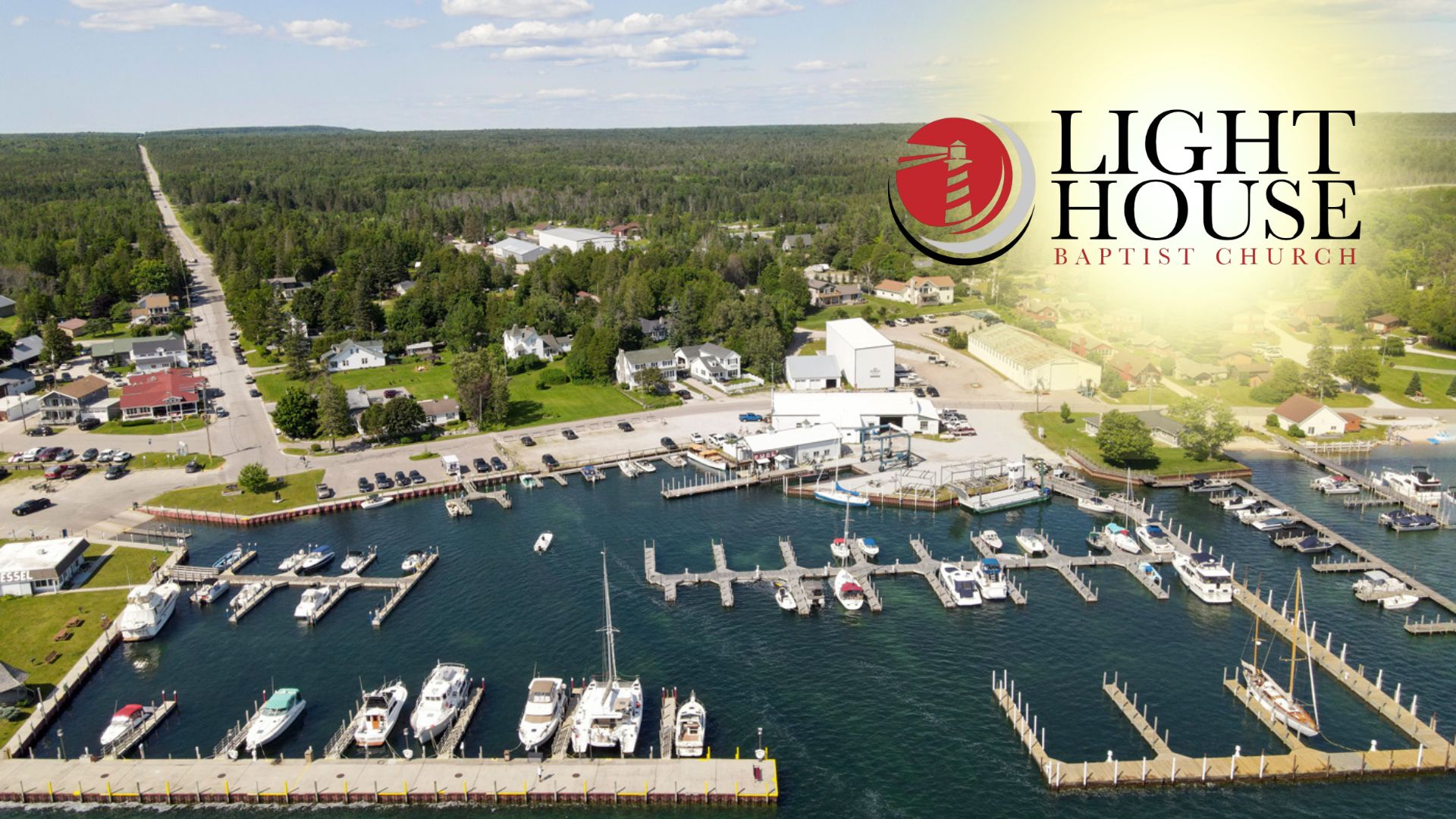 Aerial view of a marina with boats, docks, waterfront buildings, and the Lighthouse logo in the corner
