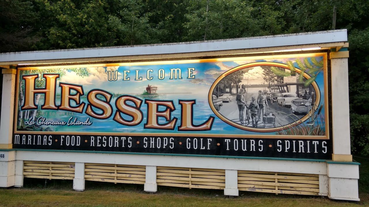 Colorful welcome sign for Hessel, listing dining, resorts, shops, golf, tours, and spirits
