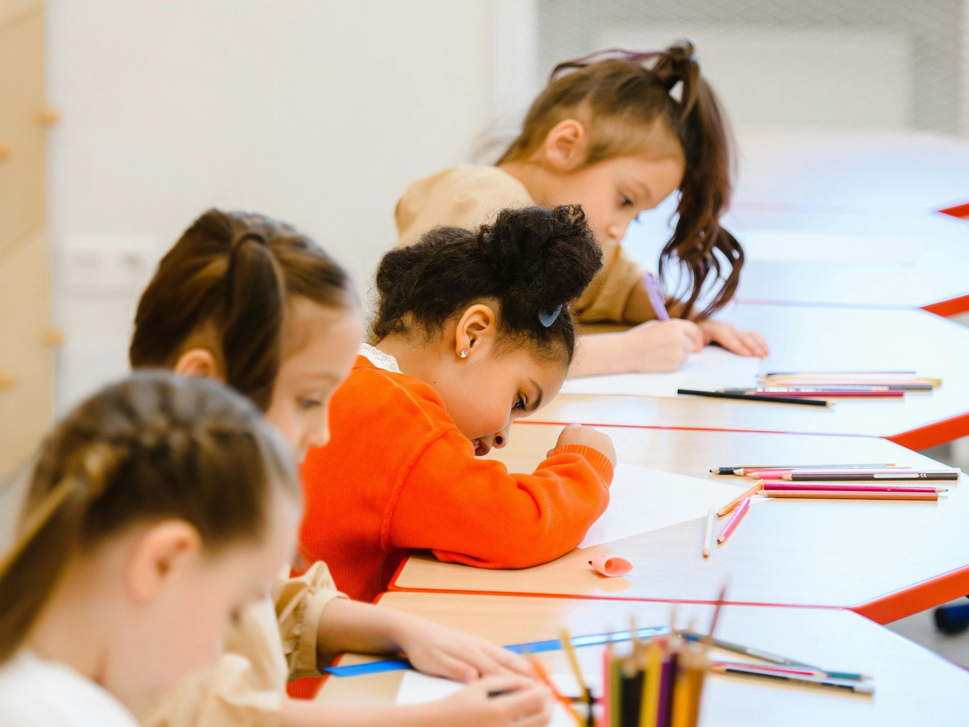 Children seated at a table, writing quietly in notebooks during a classroom activity