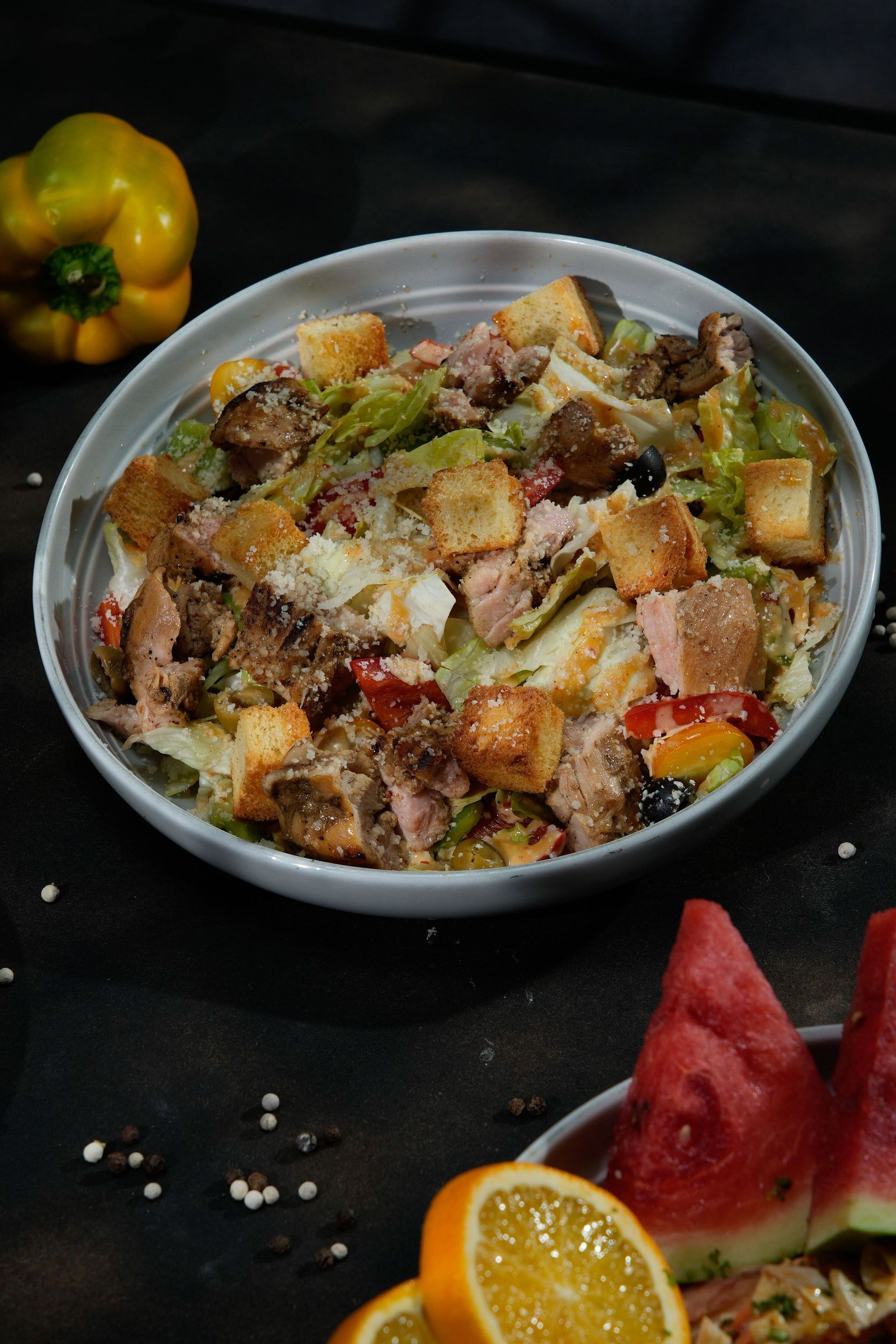 Fruit salad in a bowl with assorted diced fruit, berries, and grated cheese on a dark table with watermelon and orange slices