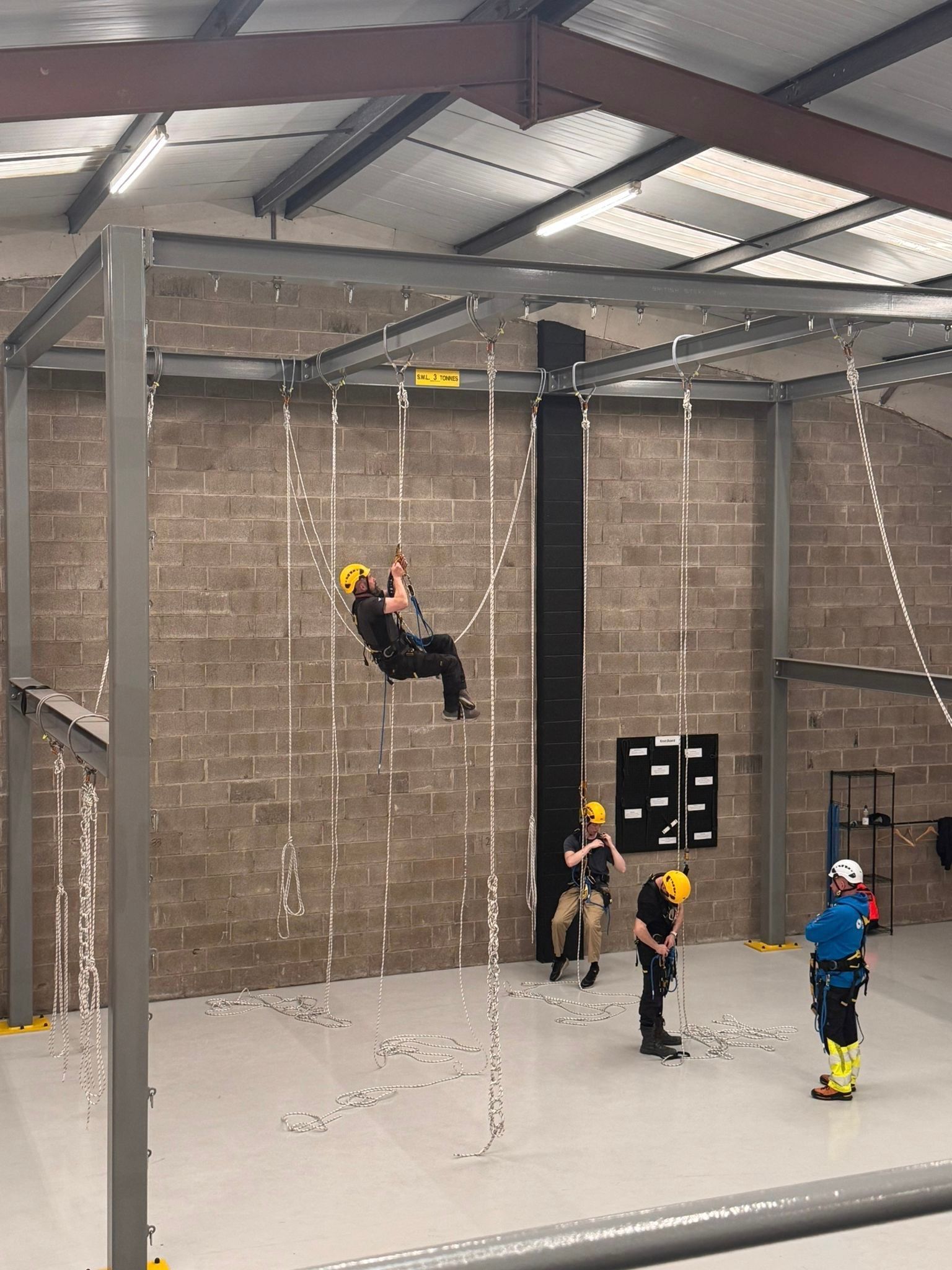 People in harnesses practice climbing on a metal structure inside Dangle Academy. Others watch and prepare.