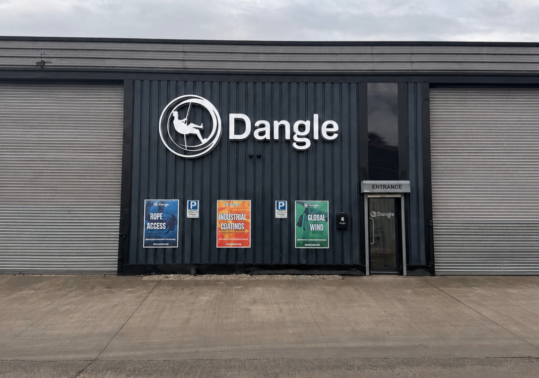 Dangle storefront with gray corrugated facade, logo sign, and colorful posters under an overcast sky