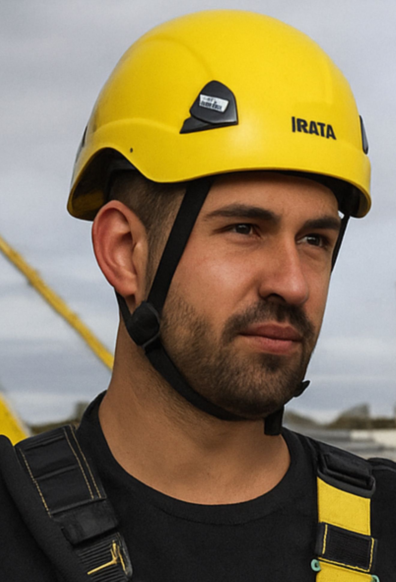 Man in a yellow helmet and harness, looking to the side. Close-up shot outdoors.