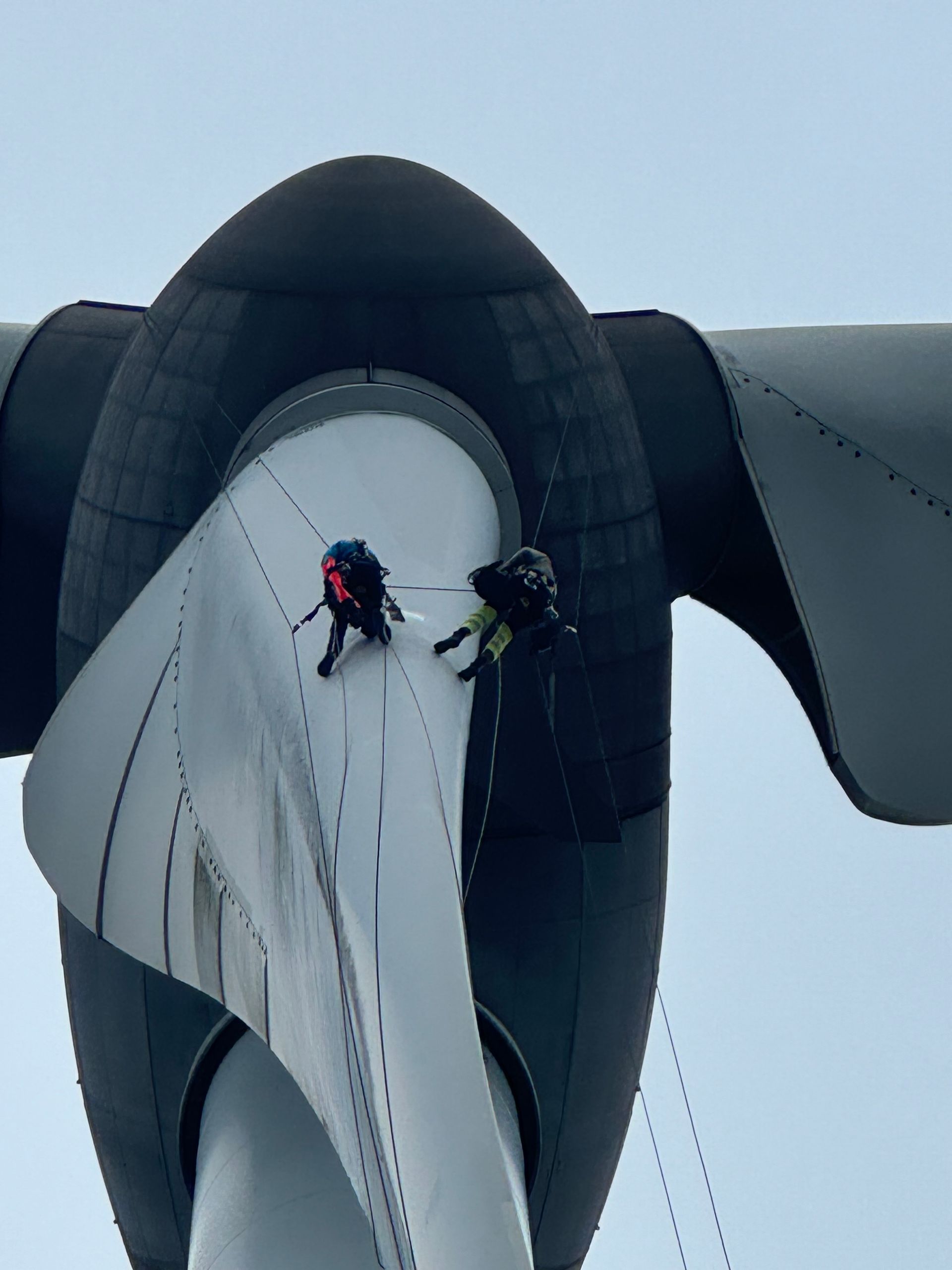 Two men are abseiling down a wind turbine blade doing wind turbine maintenance.