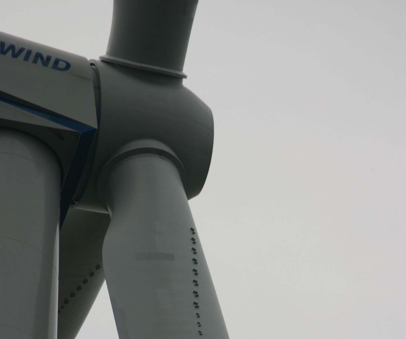 Close-up of a wind turbine's nacelle and blade in front of a cloudy sky.