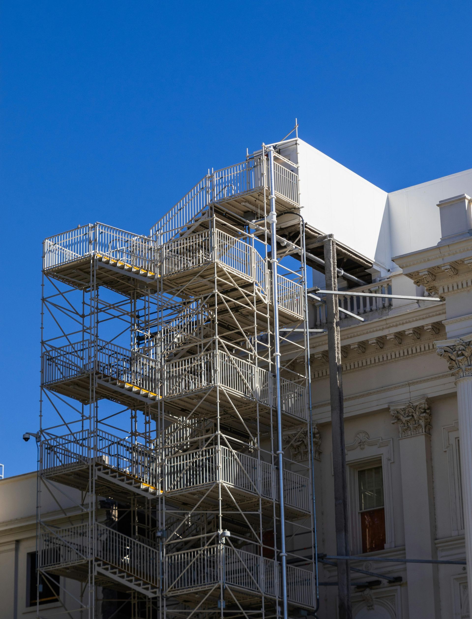 Scaffolding beside a white building against a clear blue sky in Belfast, Northern Ireland.
