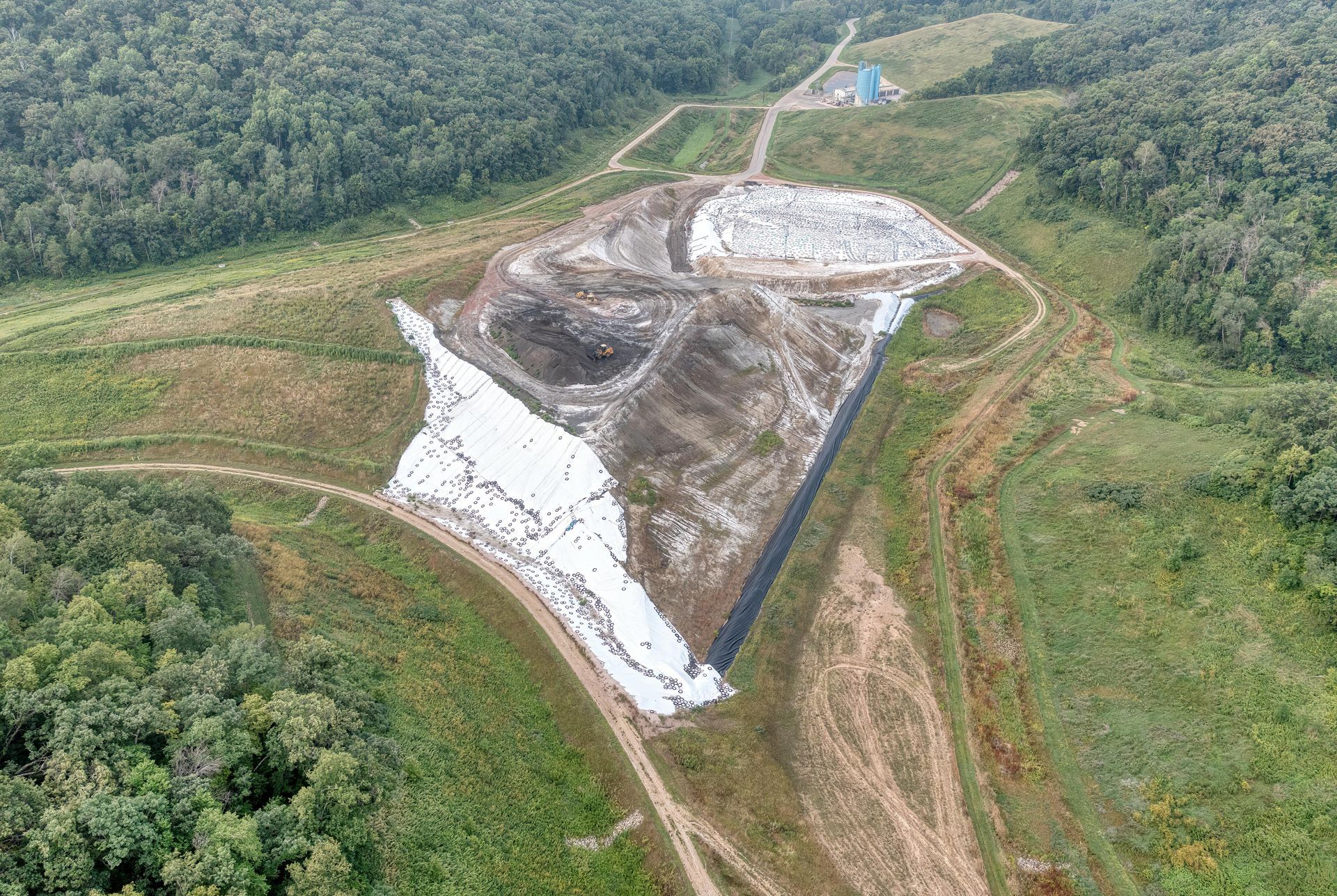 Aerial view of a landfill site in Northern Ireland, partially covered in white sheeting, surrounded by trees and roads.