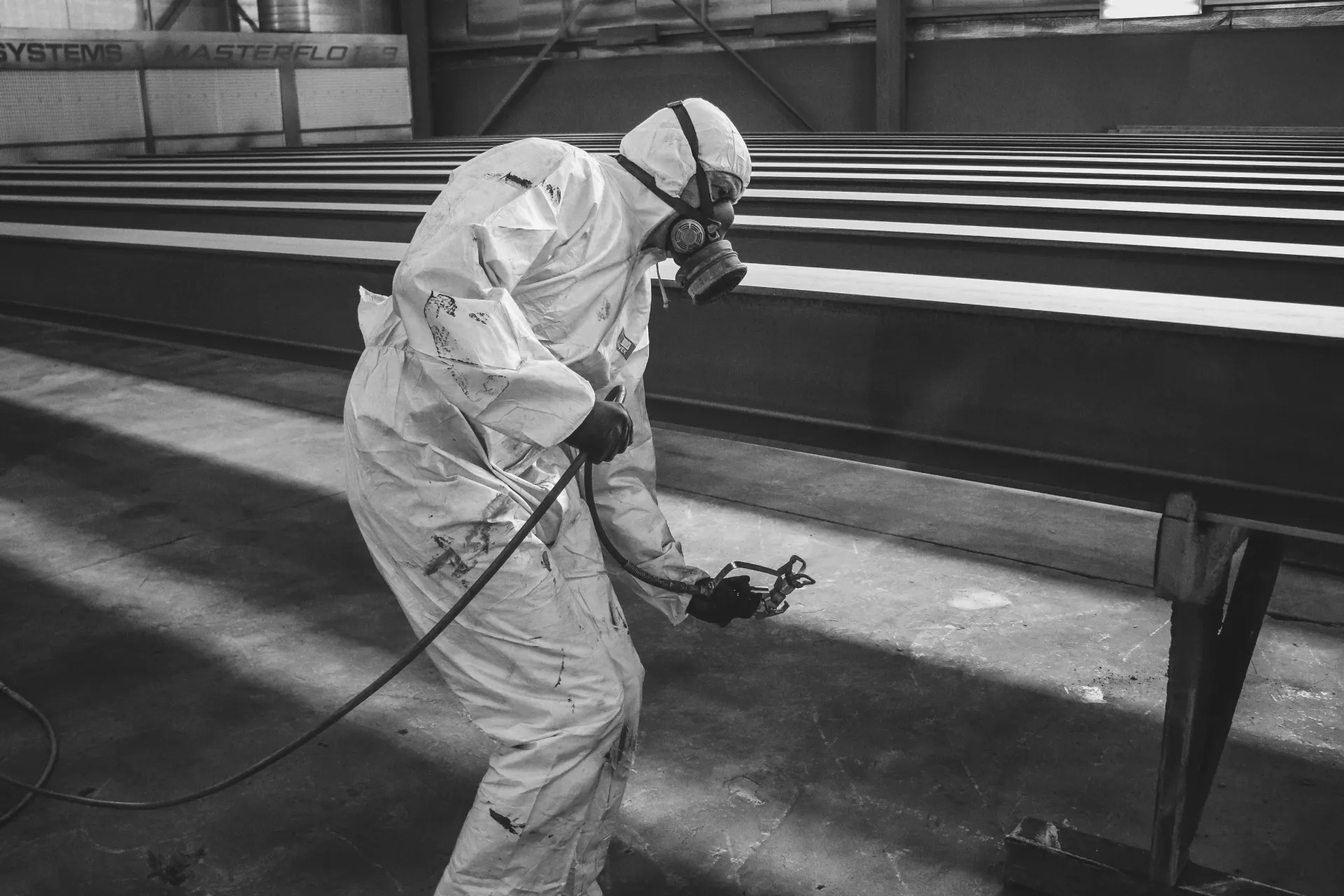 A man in a protective suit is spray painting a metal structure.