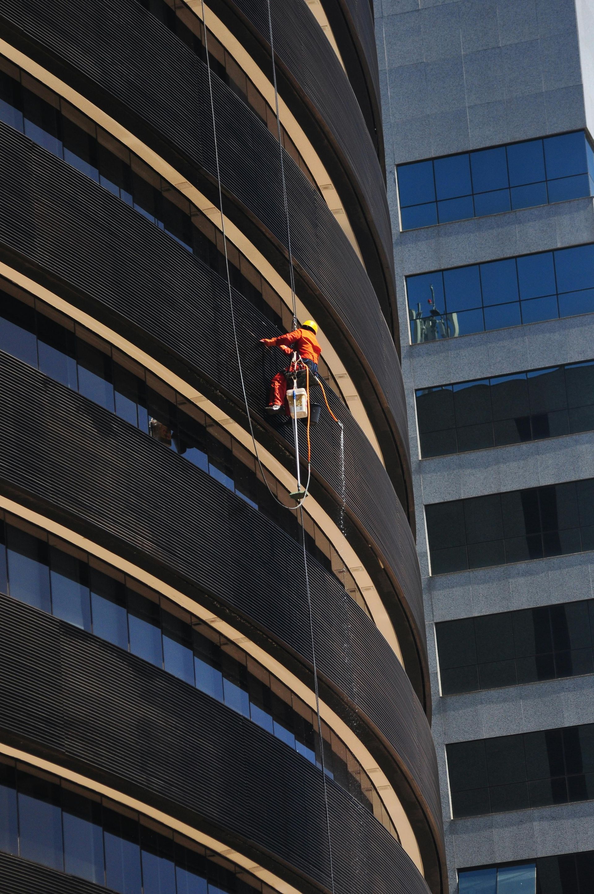 Window cleaner on a curved skyscraper, using abseiling and rappelling, rope access to clean the exterior windows.