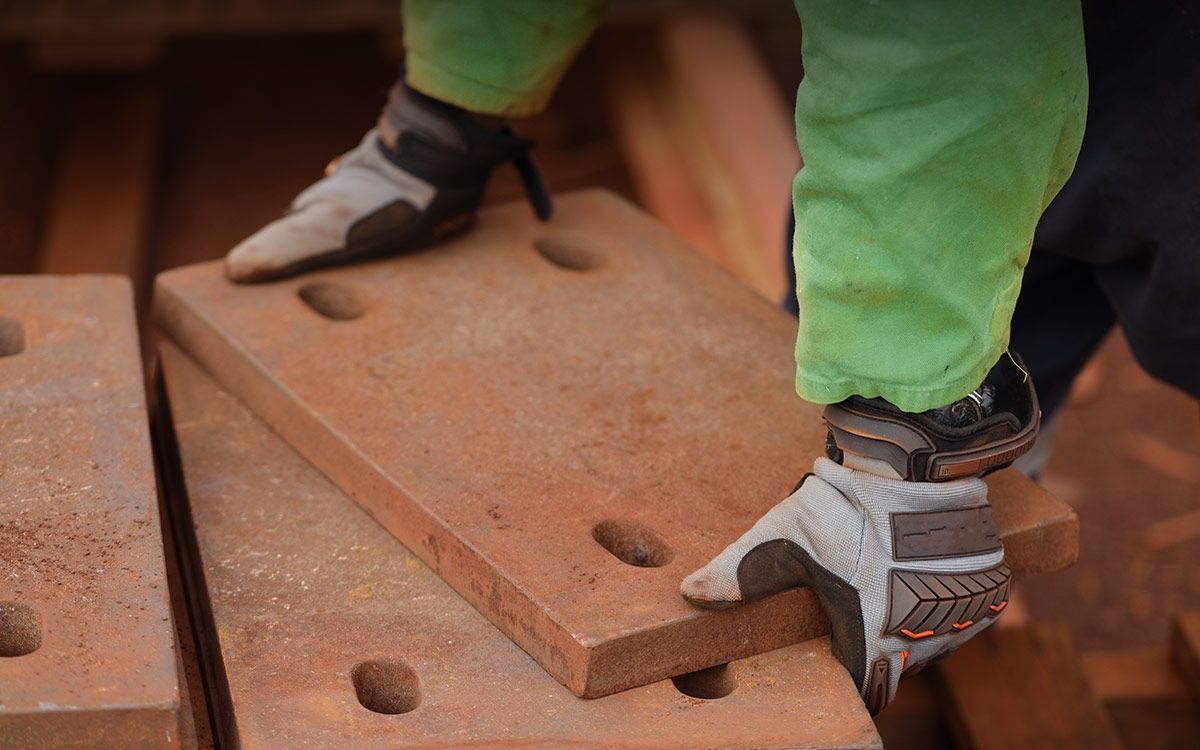 Worker in green pants and gloves handling rusty metal plates.