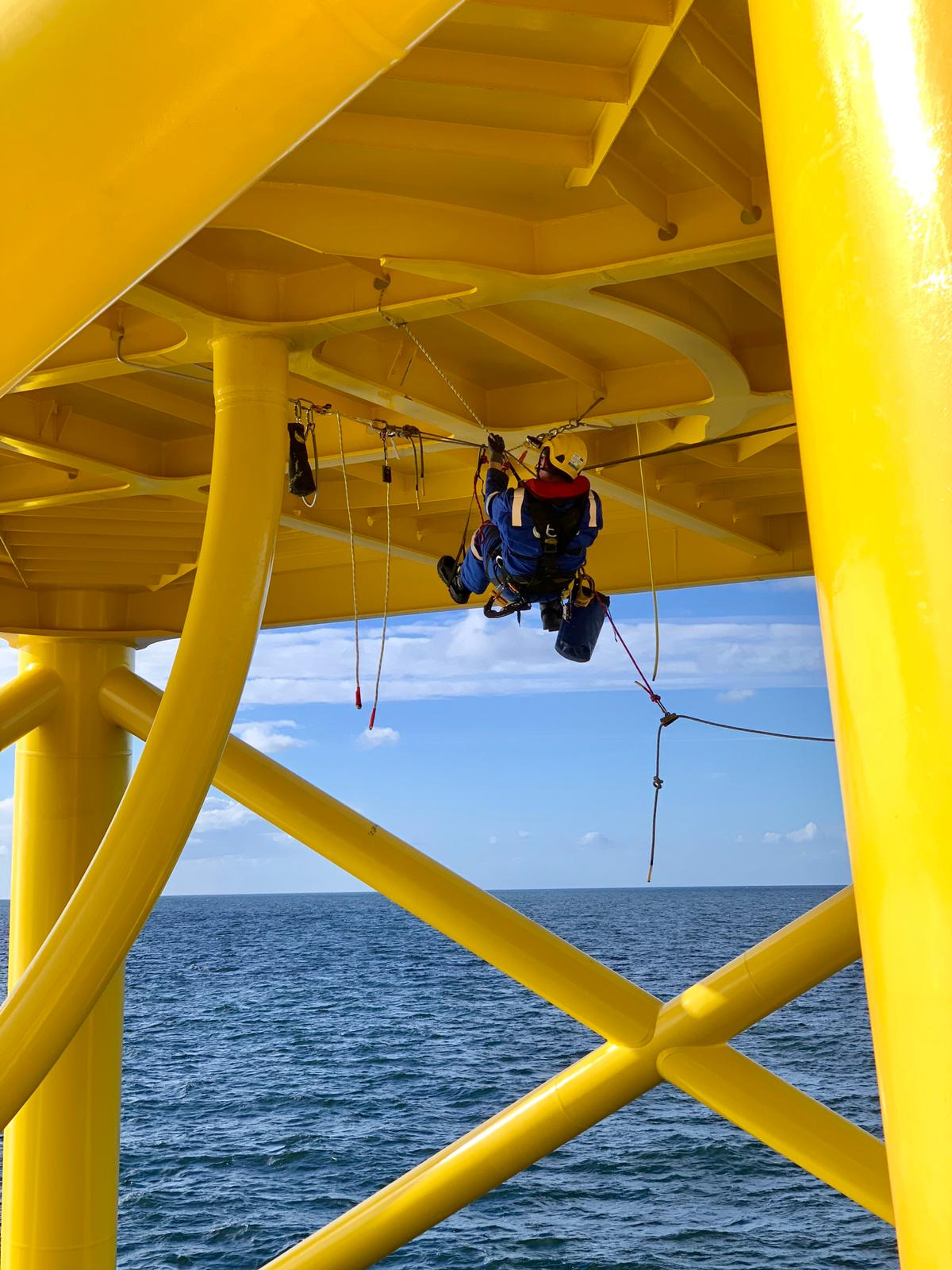 Rope access painter preparing industrial steelwork for protective coating