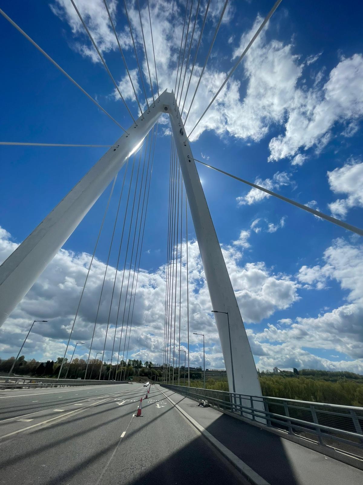 White suspension bridge against a bright blue sky with scattered clouds.